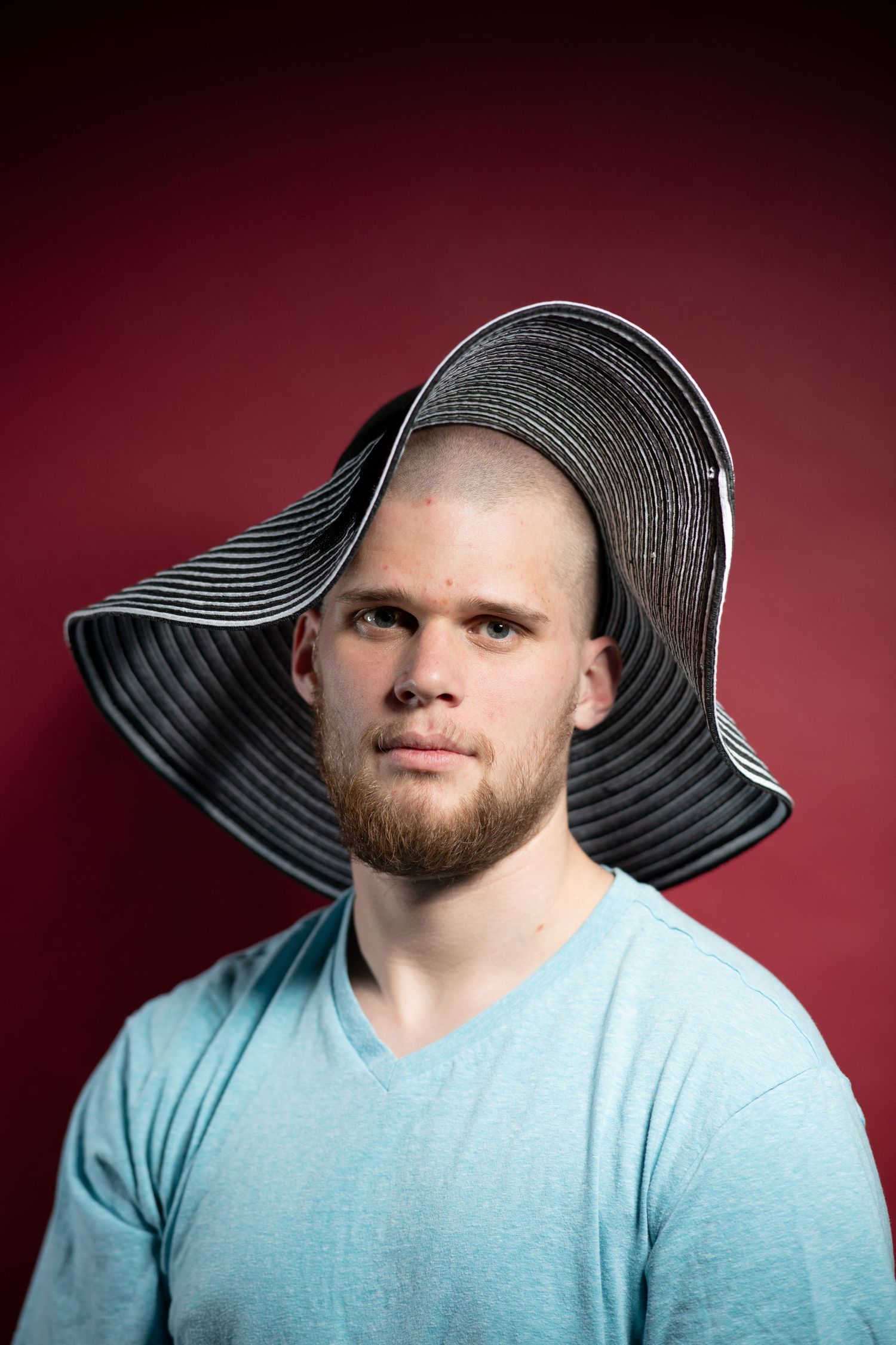 Person wearing a wide-brimmed black sun hat against a dark red background.