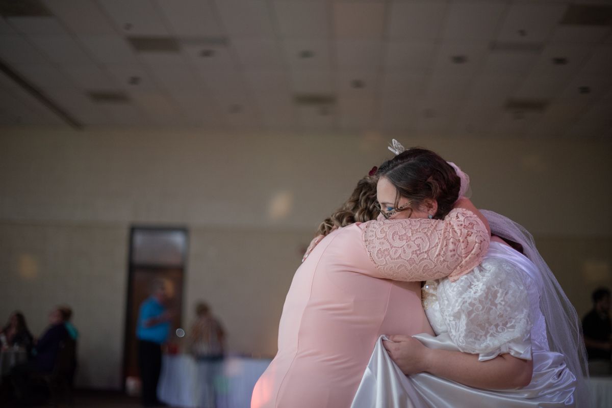 A bride and her mother embrace on the dance floor during their dance at a reception.