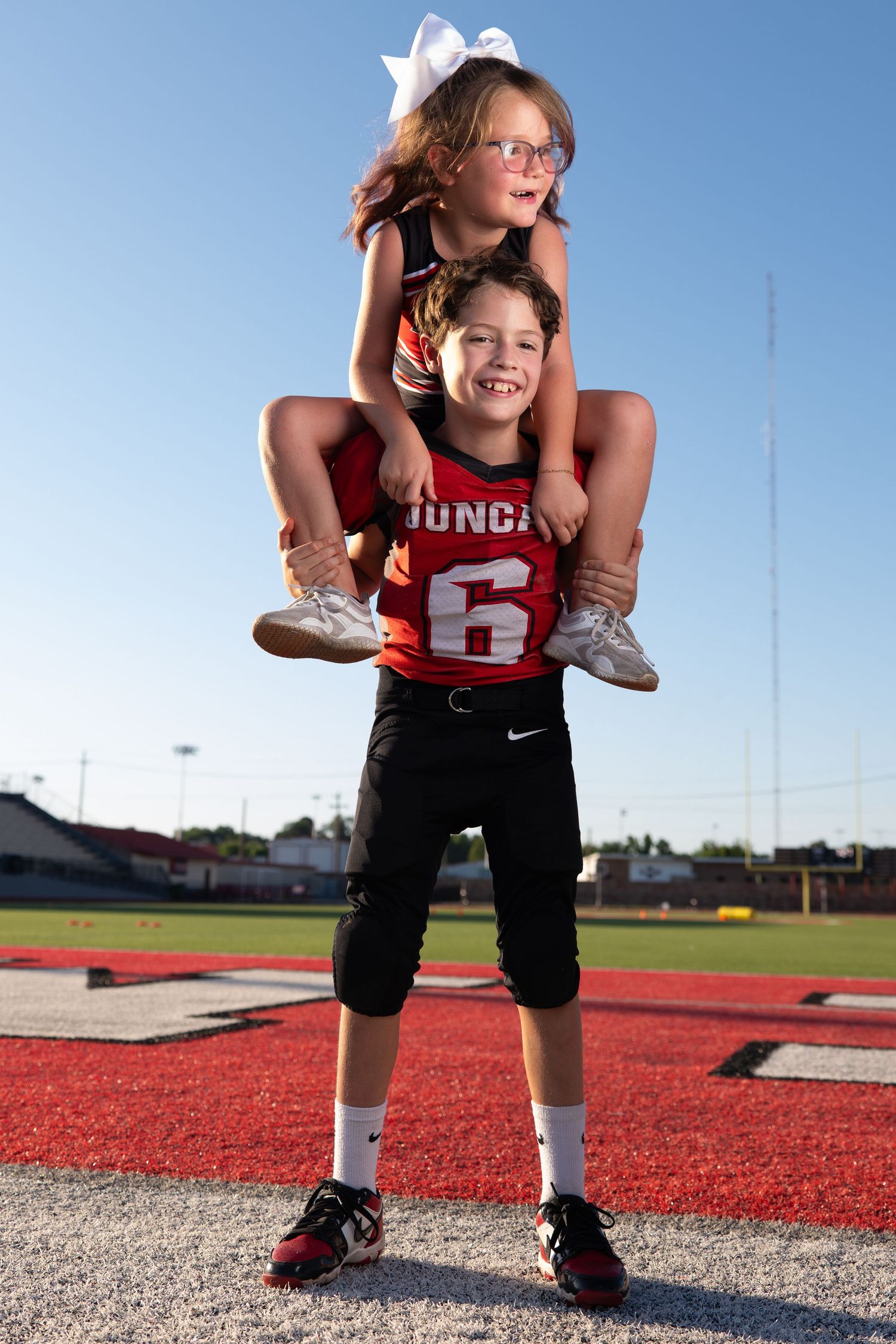 Young athlete in a red uniform holding a cheerleeder on his shoulders on a sports field.