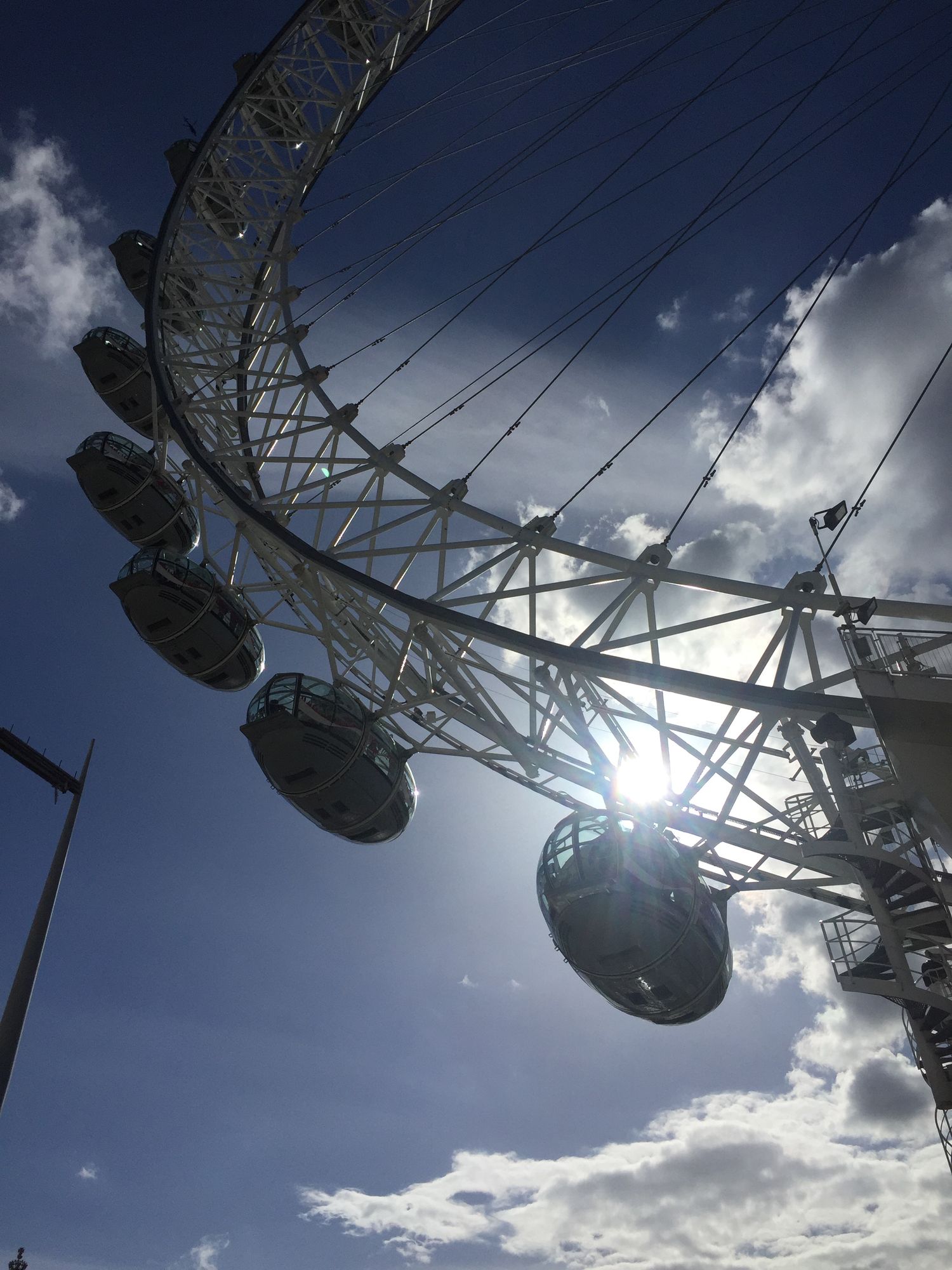 Silhouette of London Eye Ferris wheel pods against dramatic cloudy sky with sunburst.