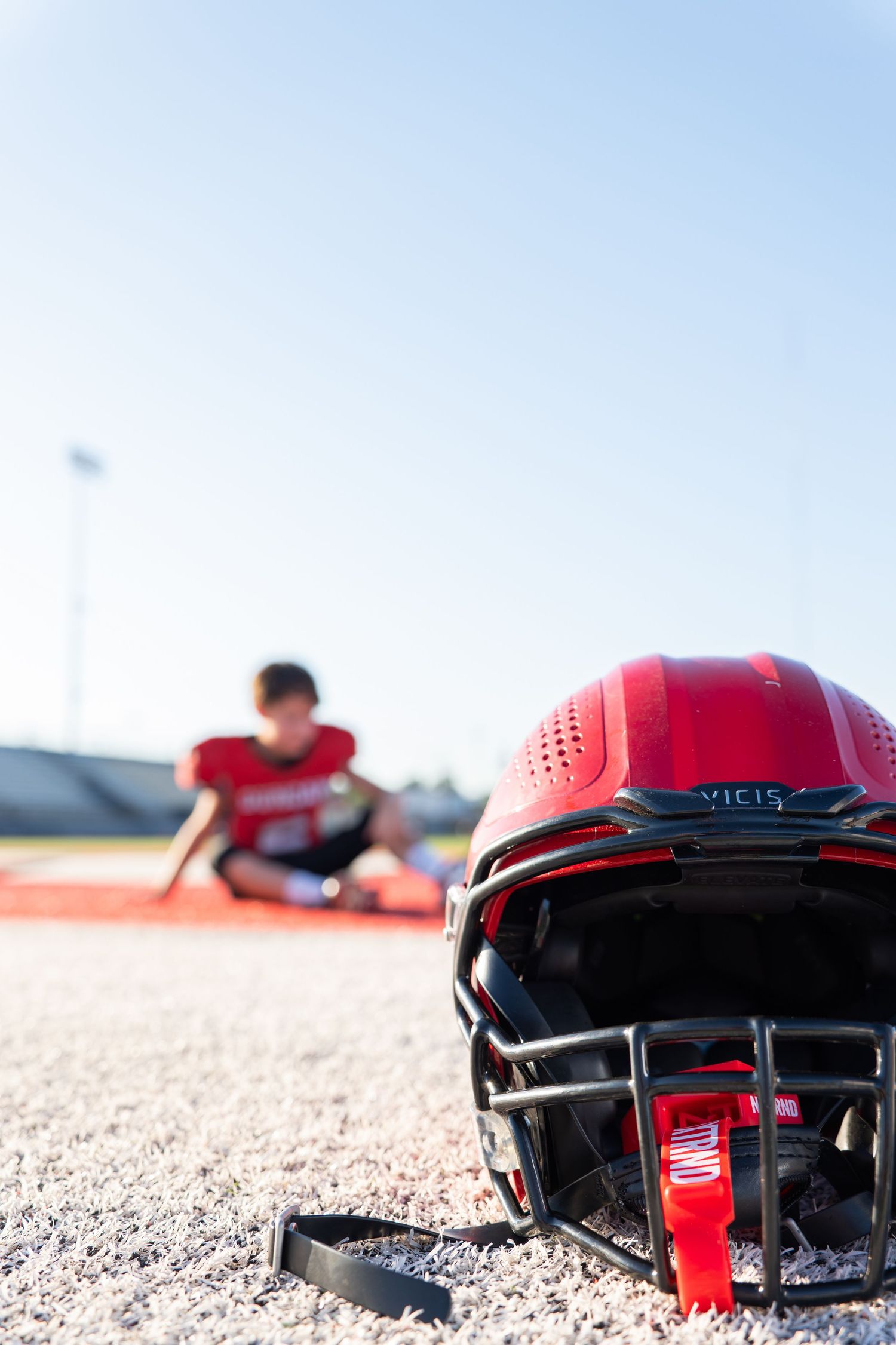 Red football helmet on a turf field with an athlete out of focus in the distance