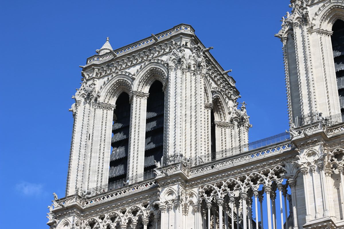 Gothic spires and towers of Notre Dame Cathedral against blue sky.