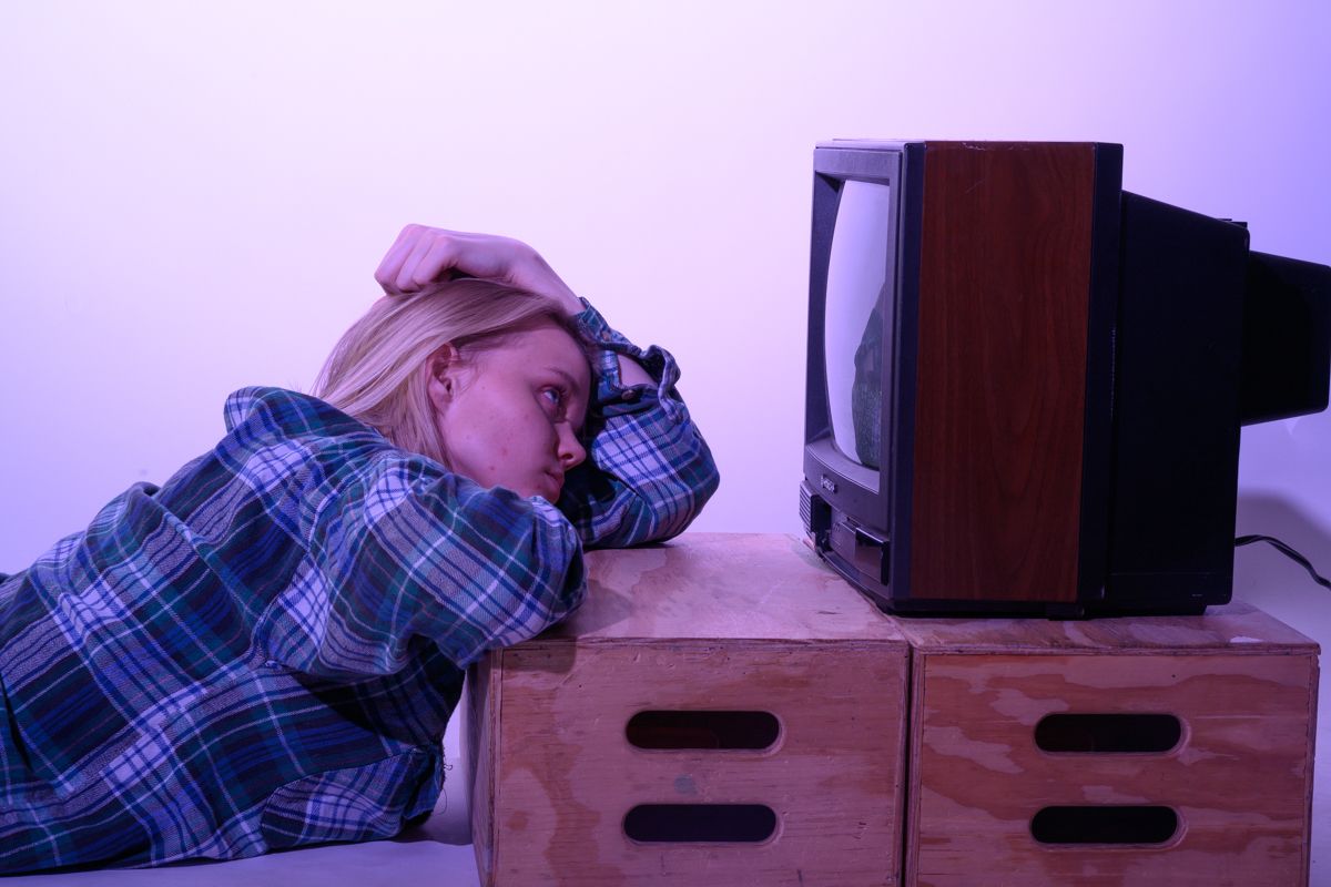 Person resting head on wooden crate in purple-tinted lighting.