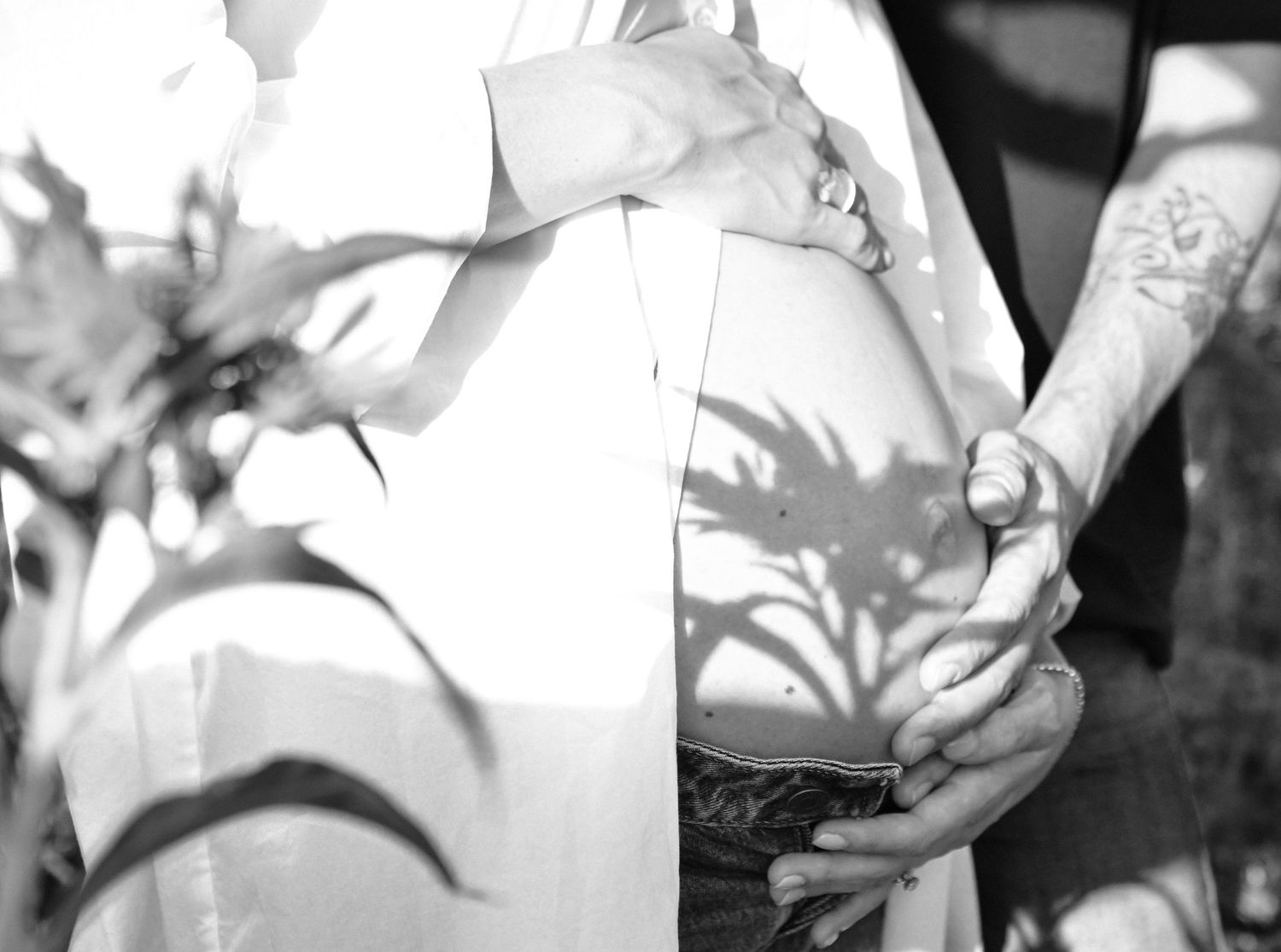 Black and white close-up photograph showing tattooed hands holding onto a white fabric in soft lighting.