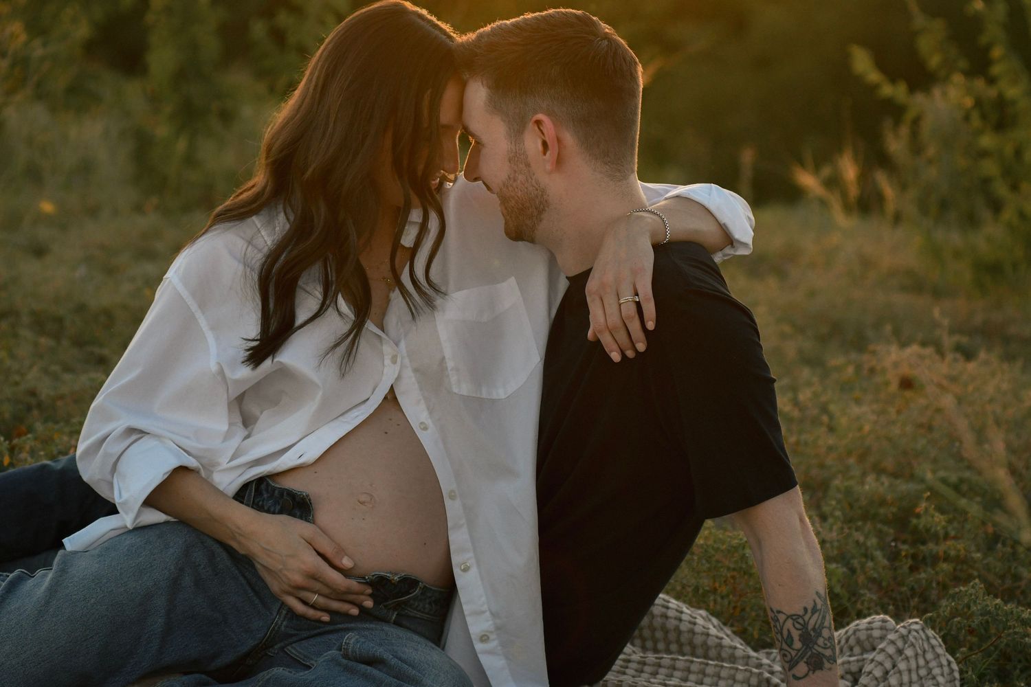 Romantic couple embraces in golden sunlit field during intimate outdoor photo session.