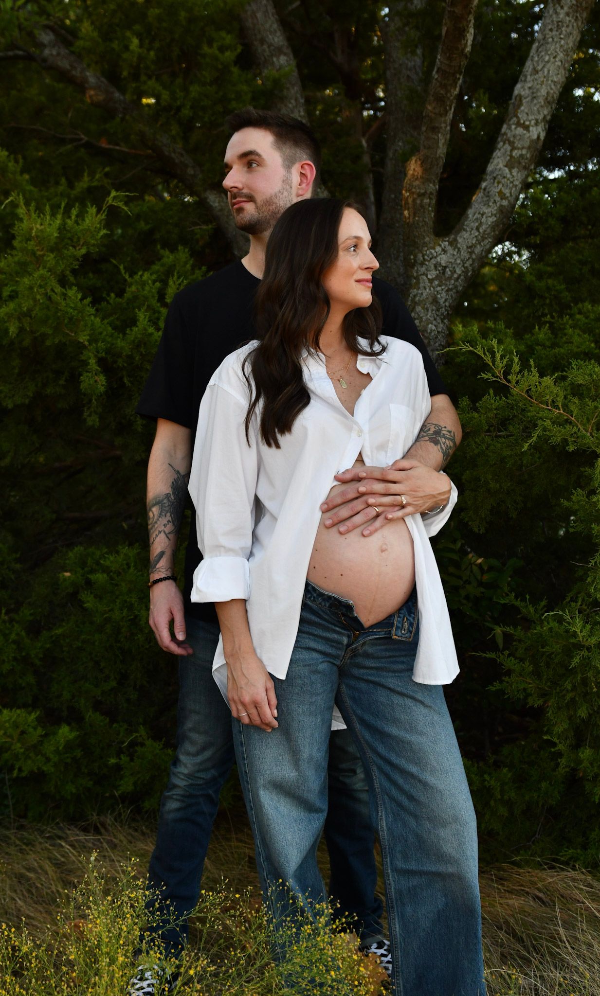 Couple in casual attire embracing outdoors against a natural green backdrop.