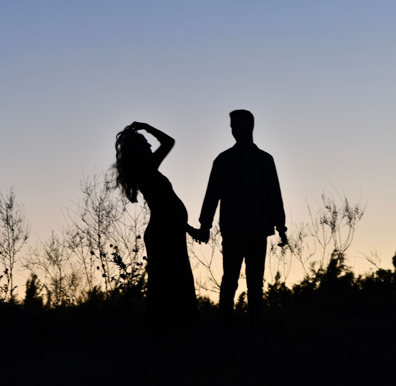 Texas photographer captures silhouettes of pregnant mom and soon to be dad walking against sunset sky.