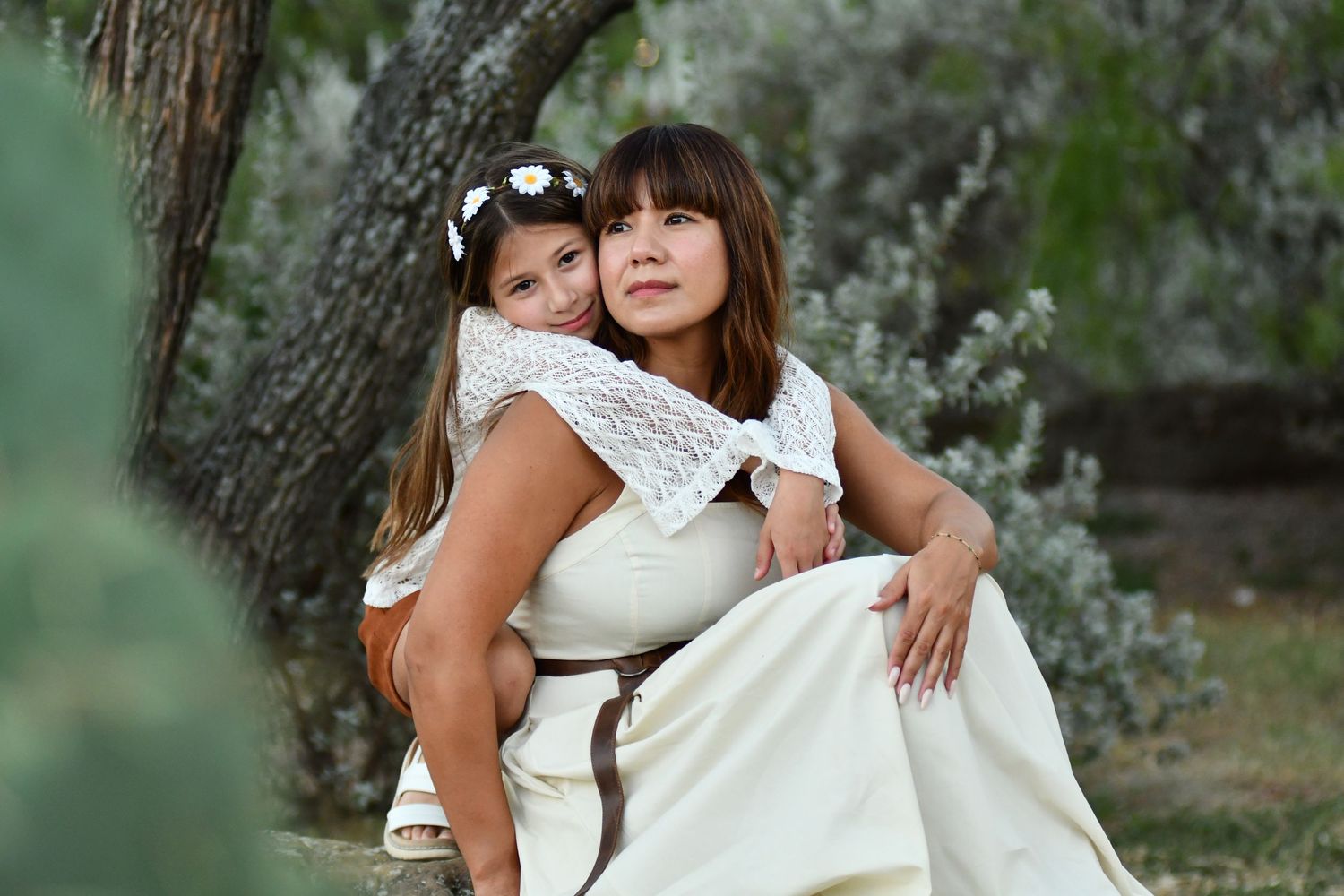A sweet mom and daughter outdoor photoshoot with white blossoms and soft sunlight creating a dreamy atmosphere.