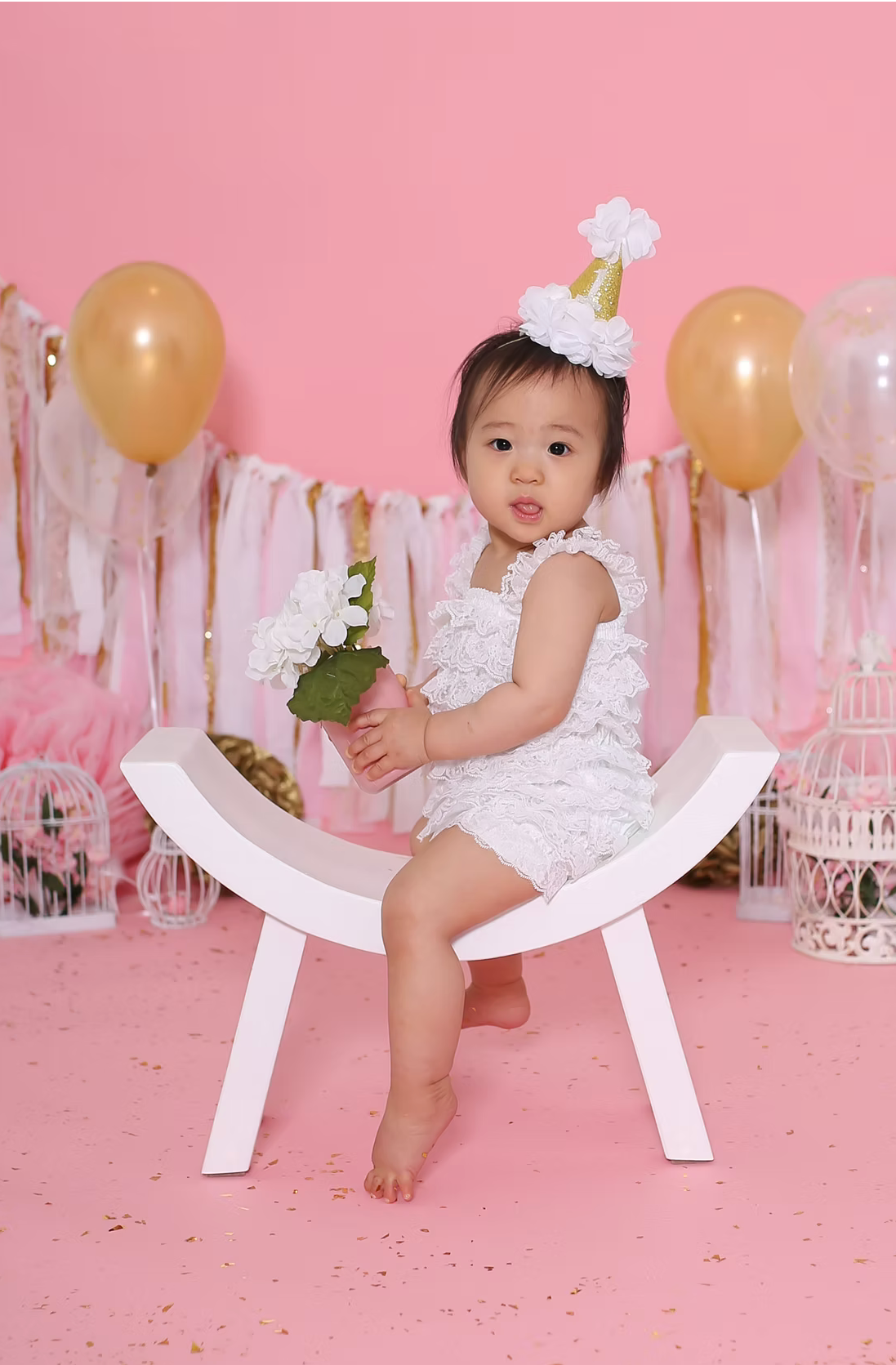 Pink cake smash photo setup with gold balloons and white streamers.