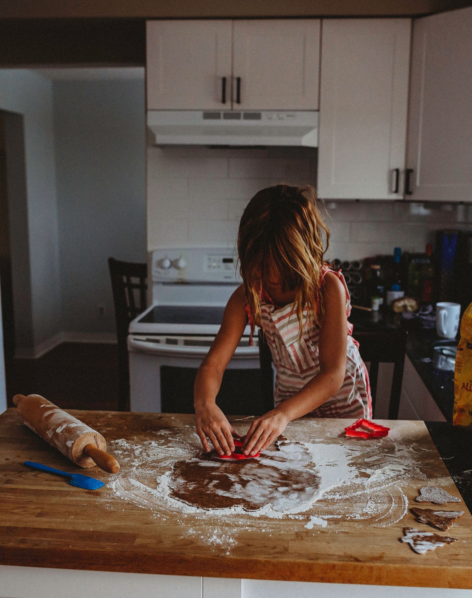 Person rolling out dough on a wooden counter in a modern white kitchen.