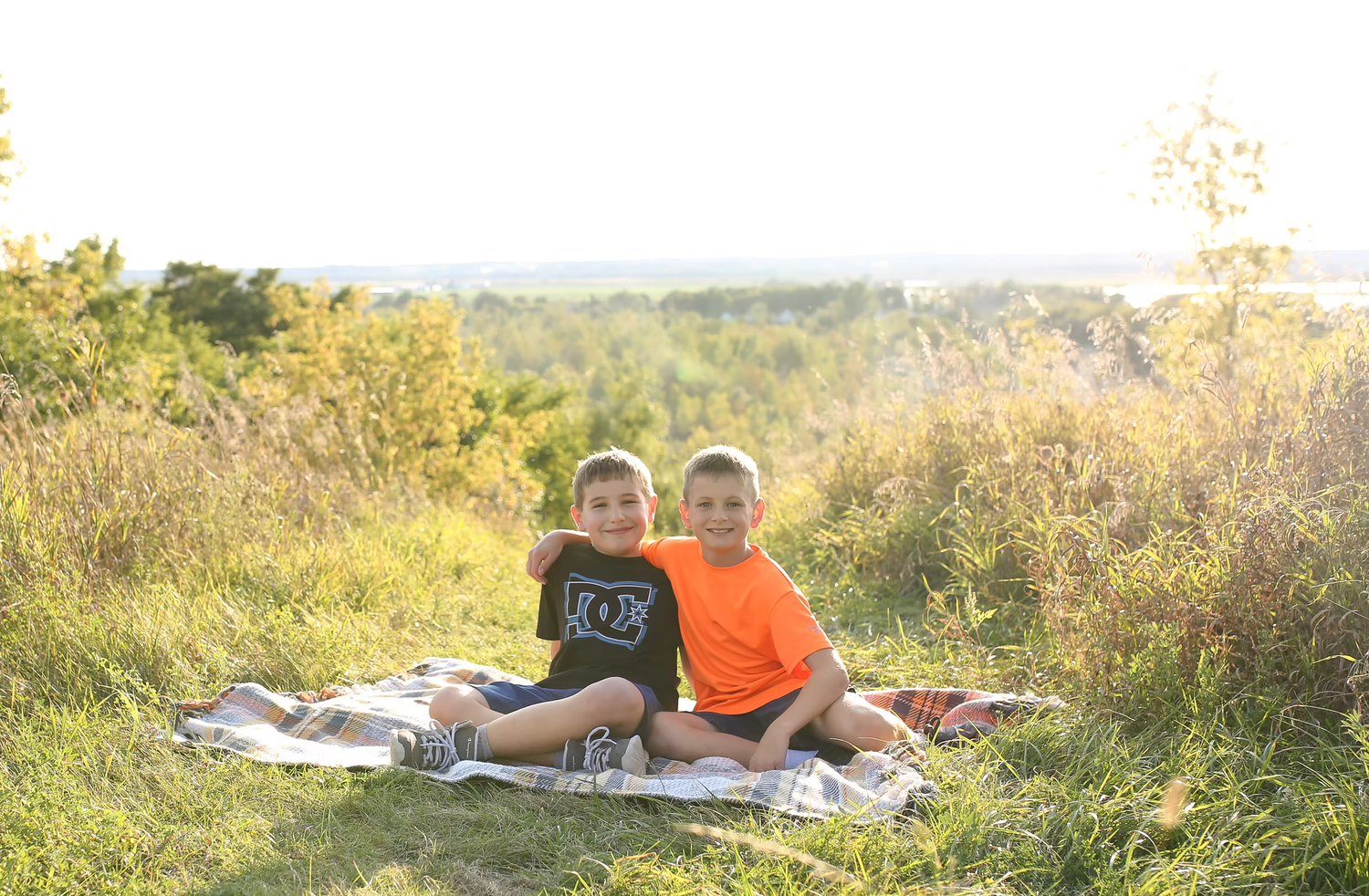 People relaxing on blanket during golden sunset in open field.