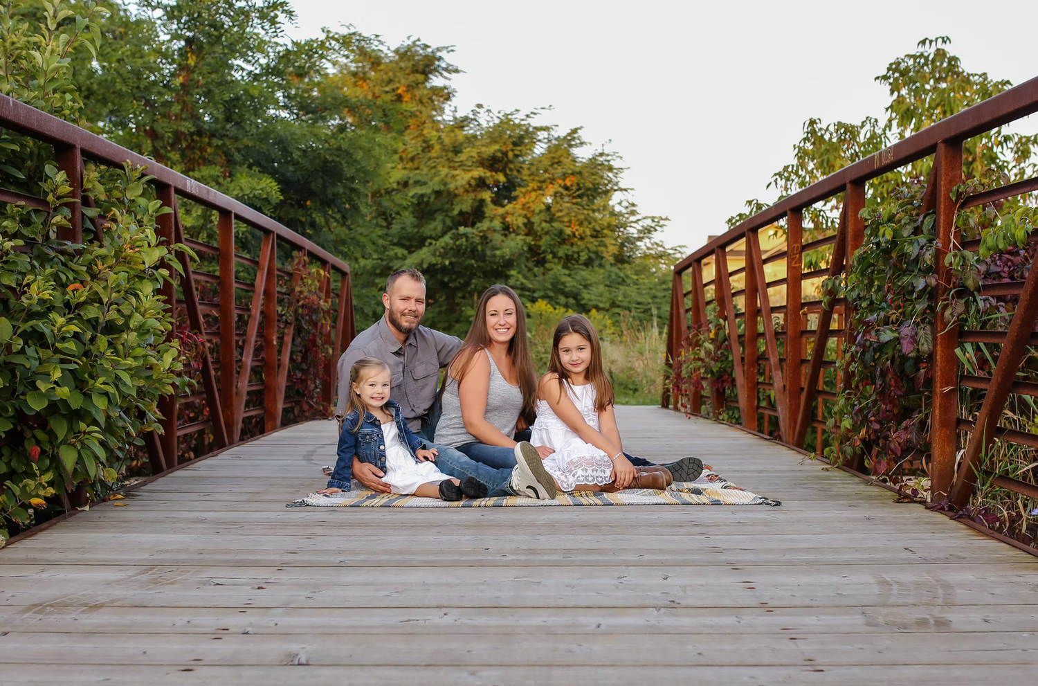 Family sitting together on rustic wooden bridge during autumn photo session.