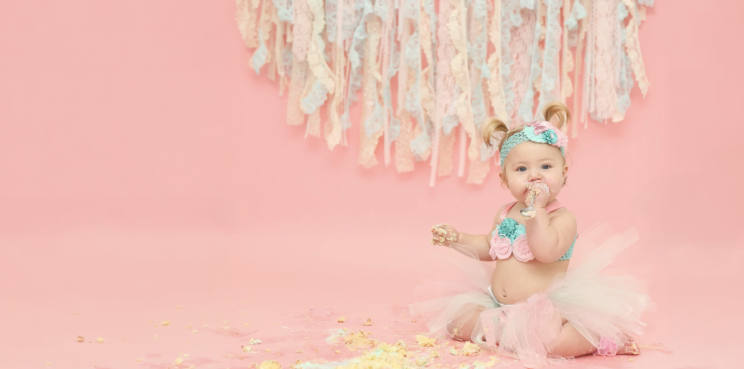 Cake smash photo setup with streamers and pink background for first birthday celebration.