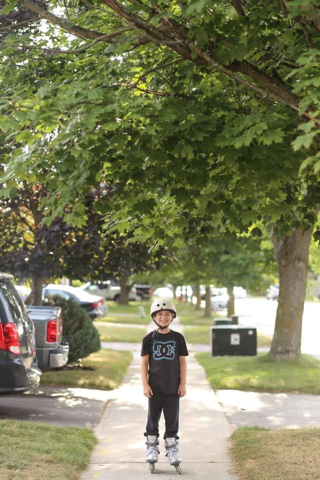 Child walking along tree-lined sidewalk on sunny summer day.