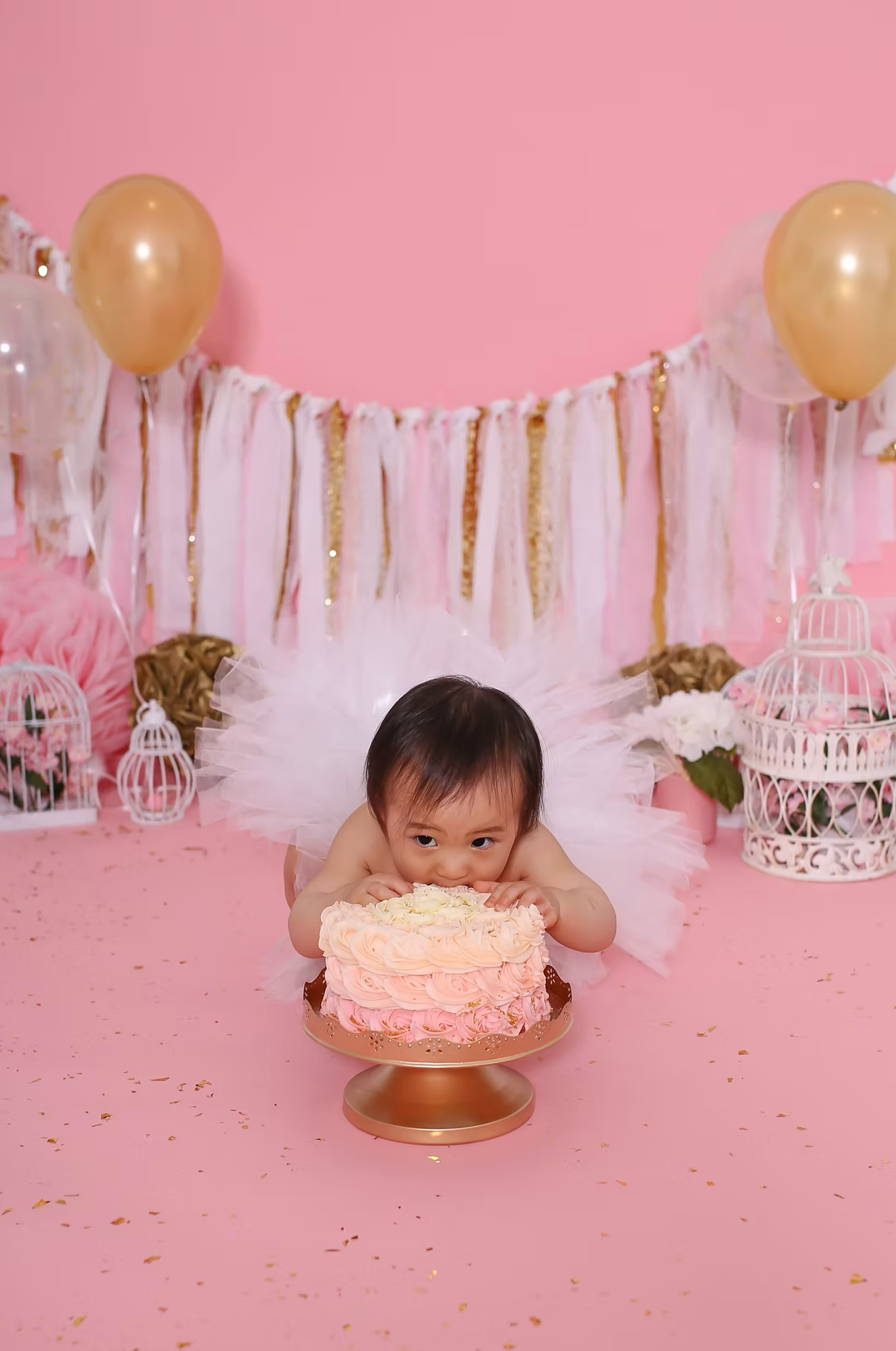 Pink cake smash setup with gold balloons and streamers for first birthday celebration.