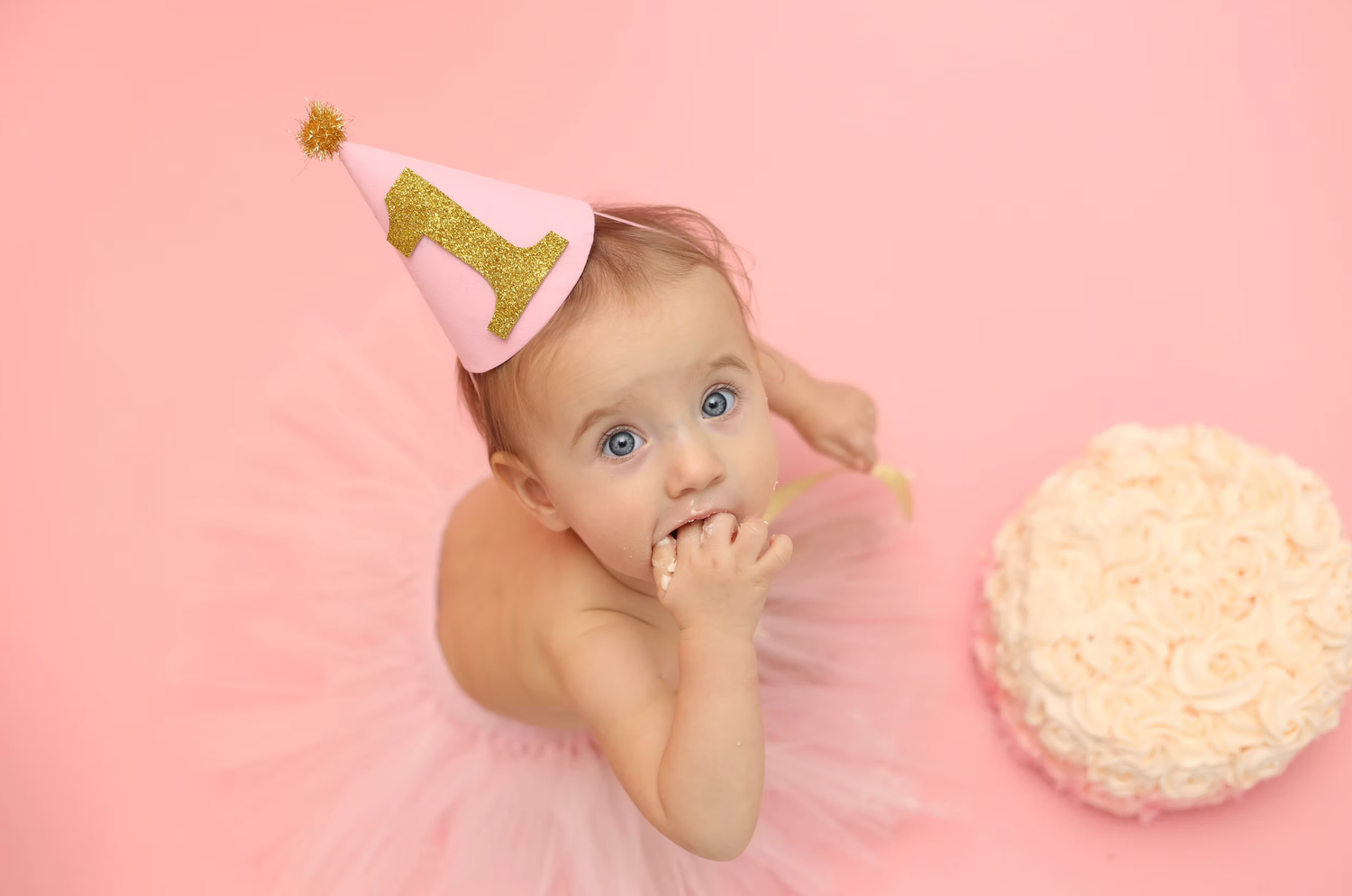 Baby cake smash photo session with pink background and white frosted cake.