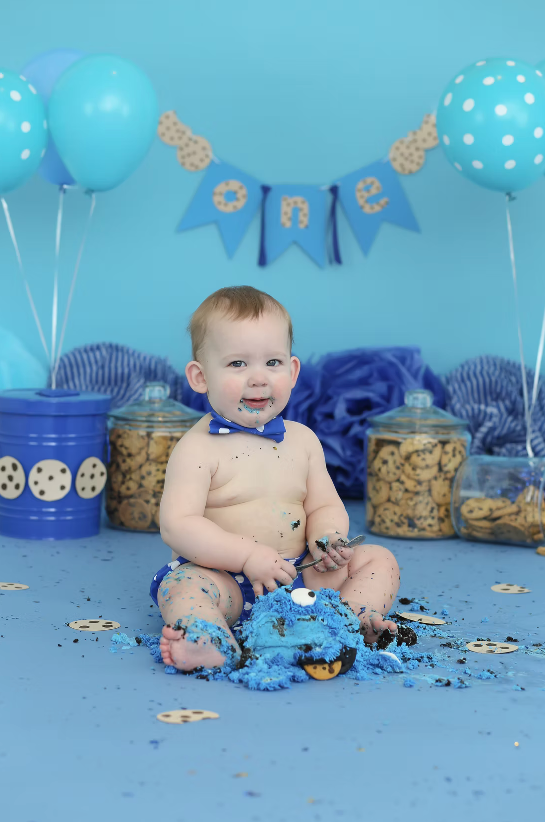 Blue themed cake smash photo setup with polka dot balloons and cookie decorations.