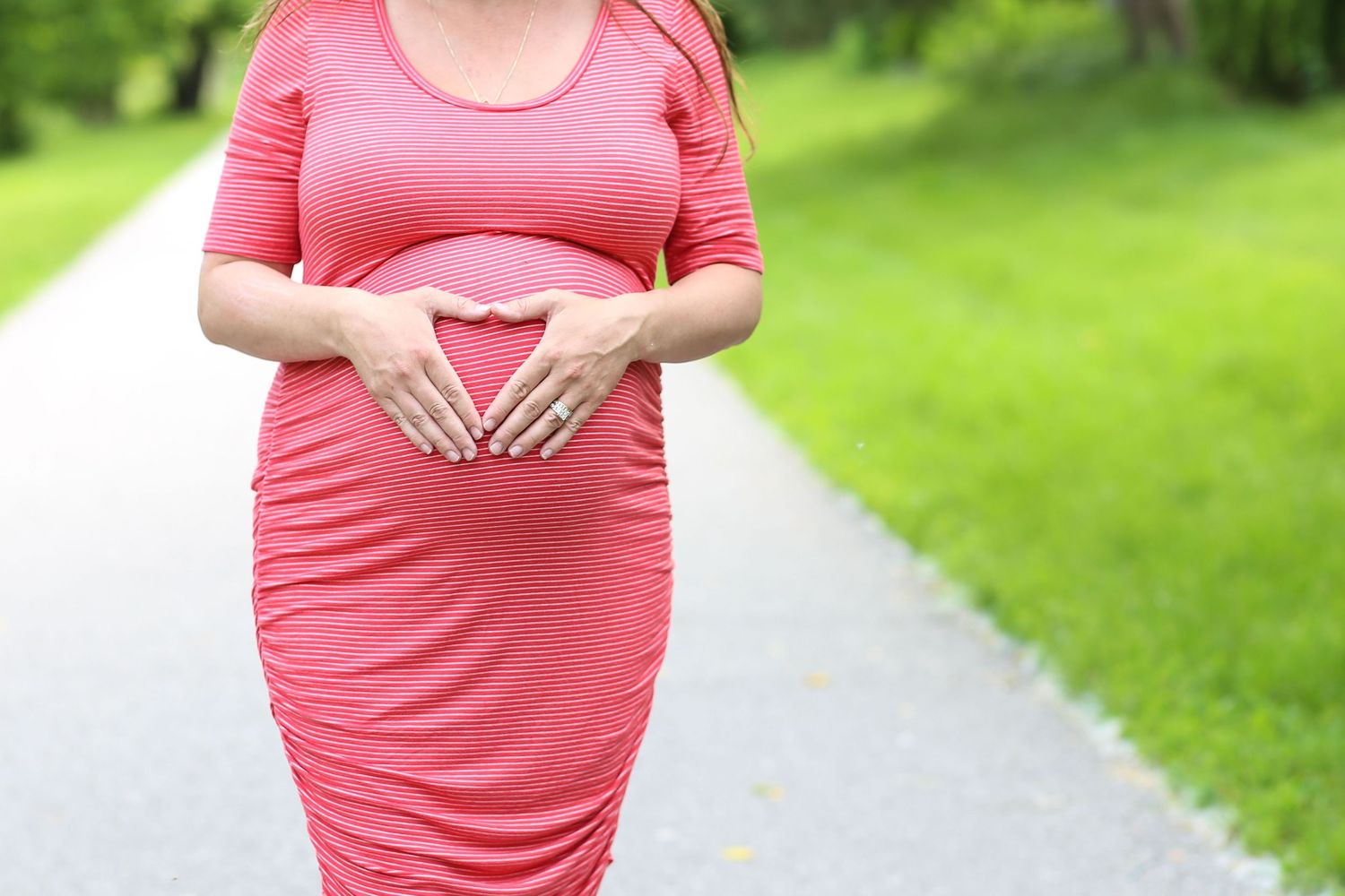 A progression of maternity photos showing a growing baby bump in a coral pink dress against a green outdoor backdrop.