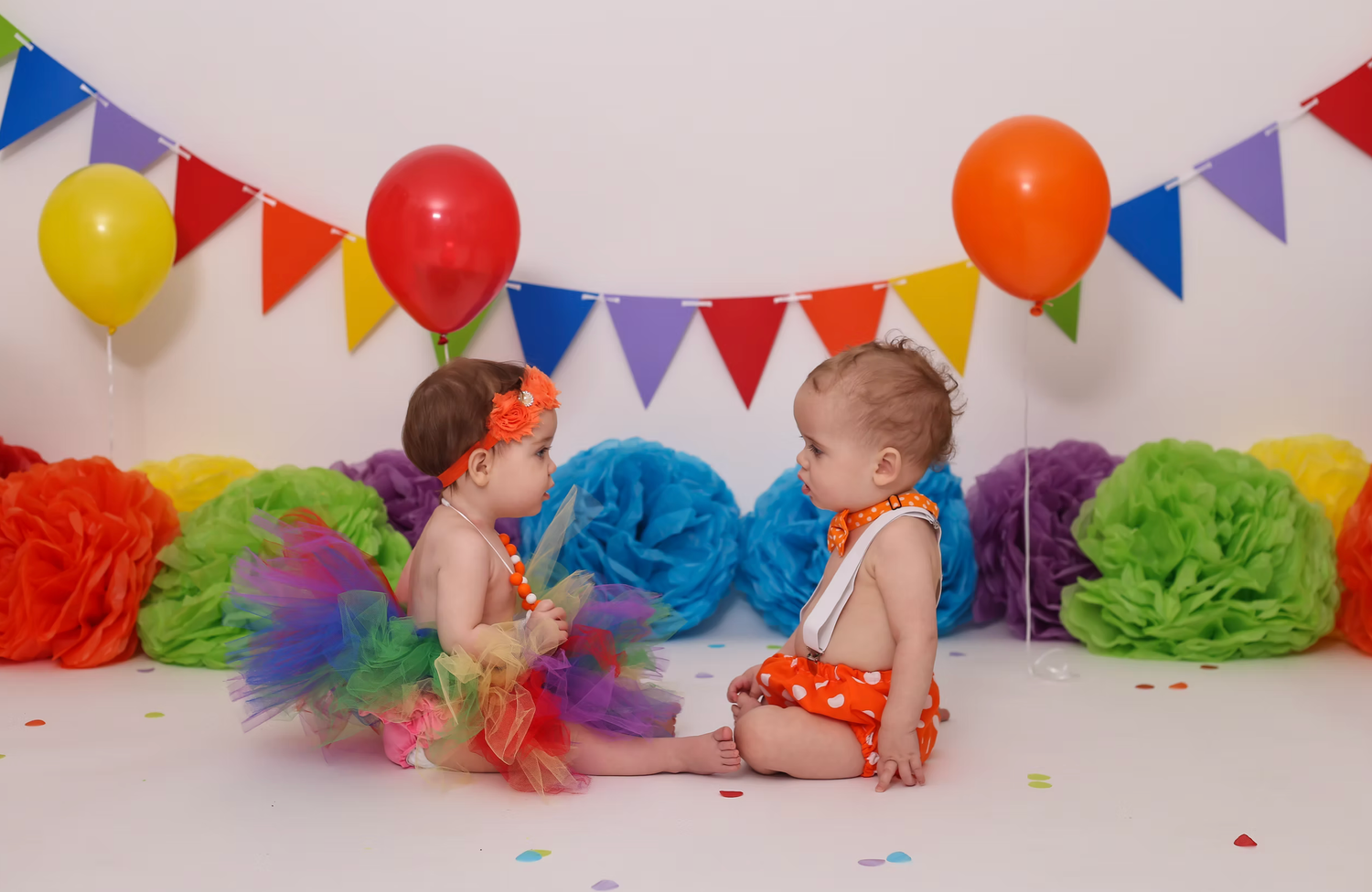 Colorful bunting flags and tissue paper pom poms create a festive rainbow party backdrop.
