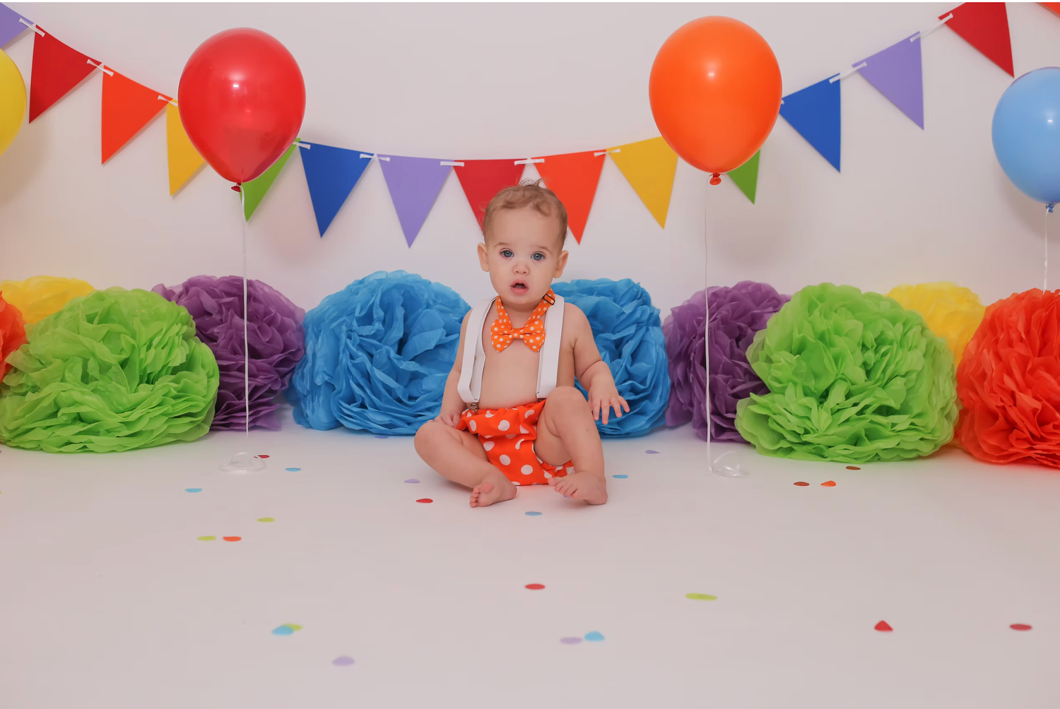 Colorful birthday backdrop with rainbow tissue poms and triangle bunting flags.