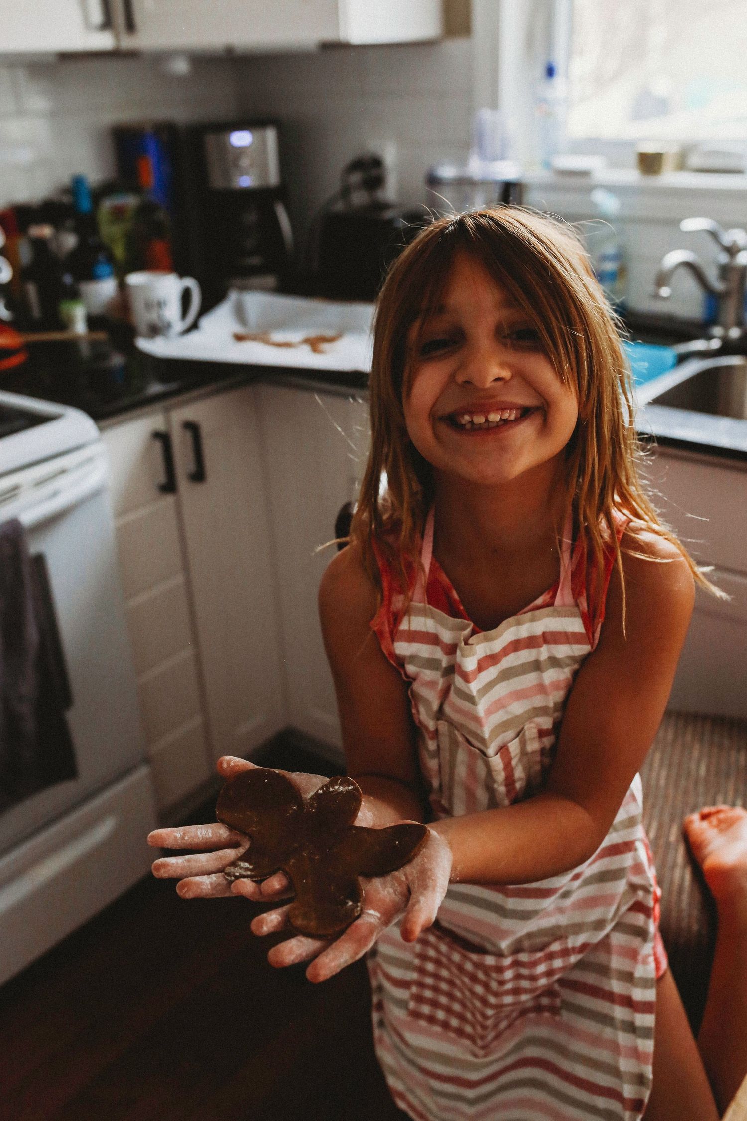 Child in red and white striped apron enjoying chocolate treats in a kitchen.