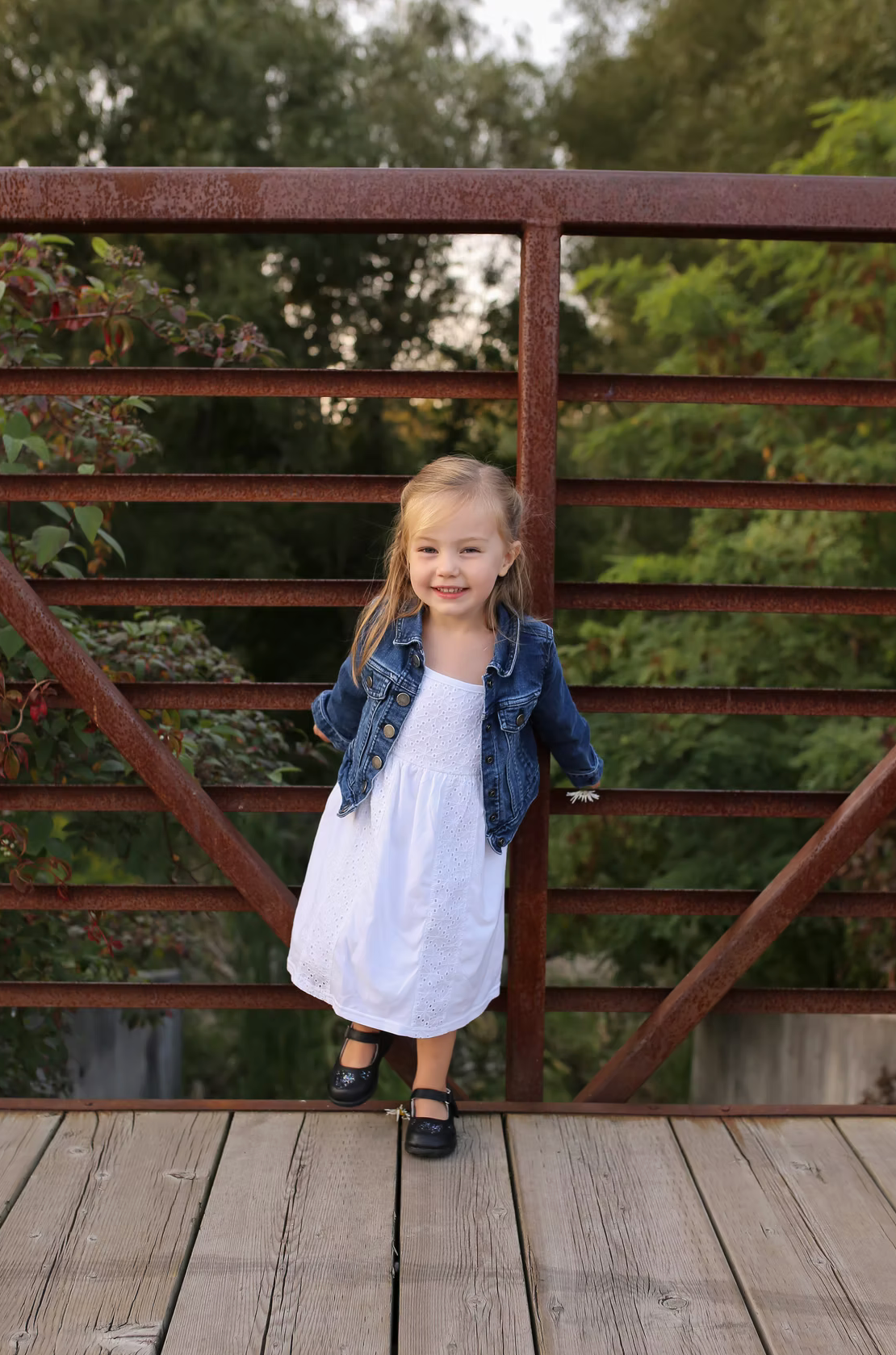 Child in denim jacket posing on rustic wooden bridge.