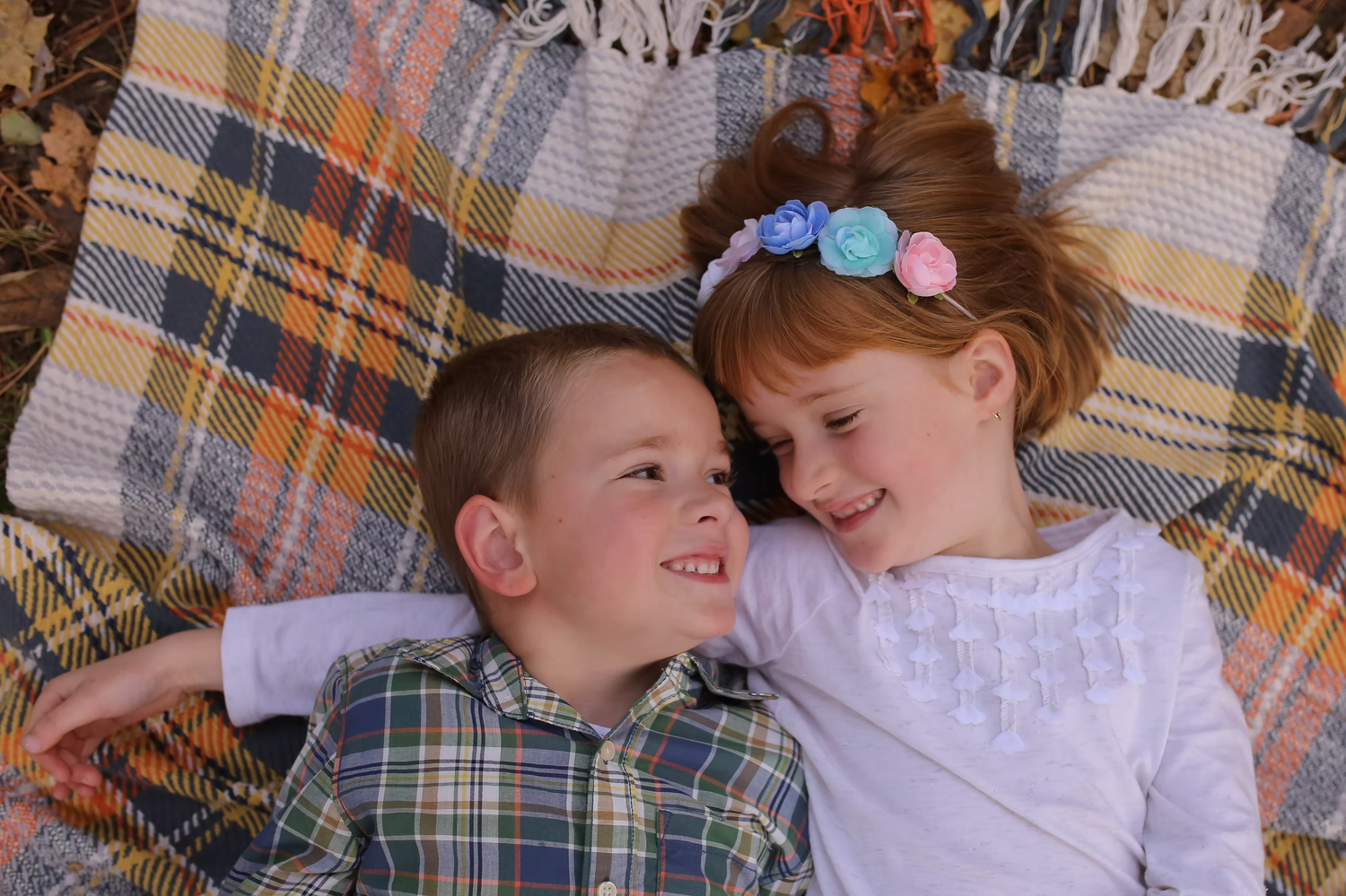 Playful autumn photo session with people laying on a plaid blanket surrounded by fallen leaves.