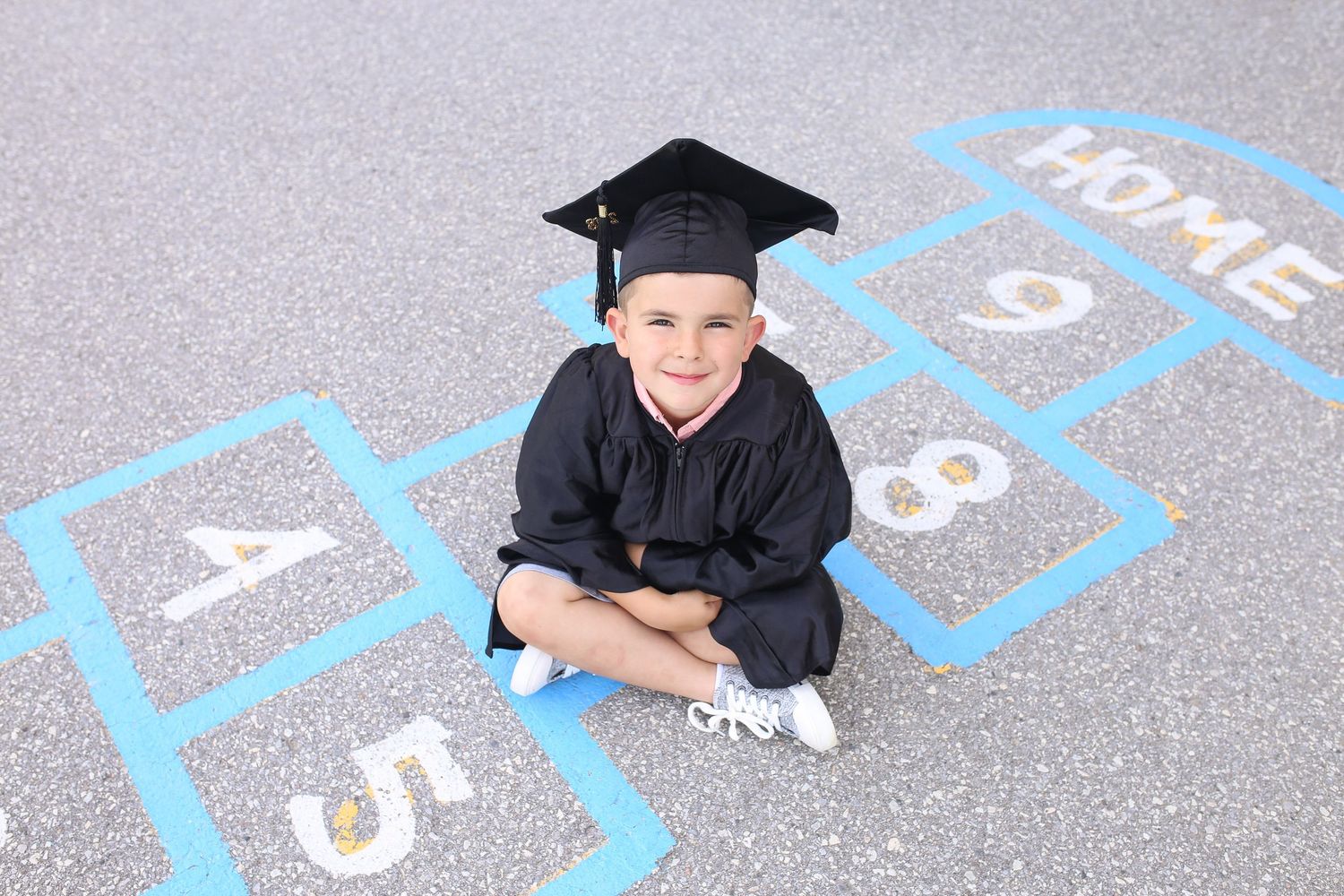 Graduate lying on painted numbers on concrete wearing a black cap and gown.