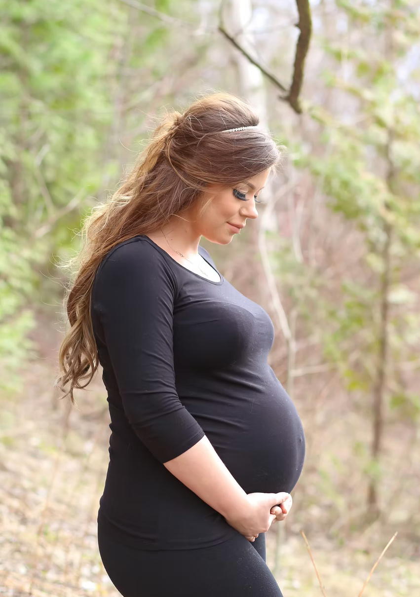 A natural outdoor maternity session with a person in black against a wooded backdrop.