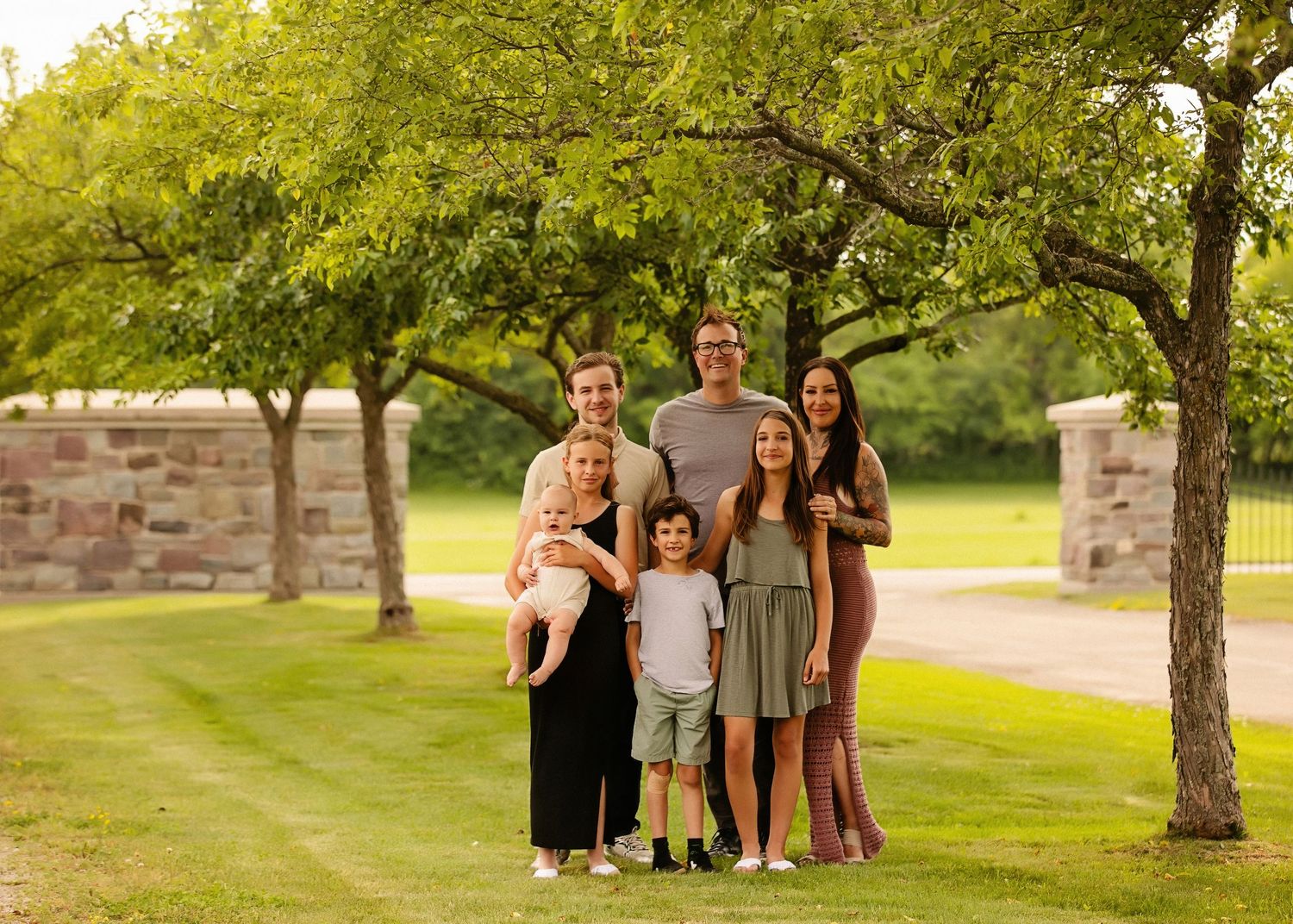 Outdoor family portrait session in a grassy park setting with trees during golden hour.
