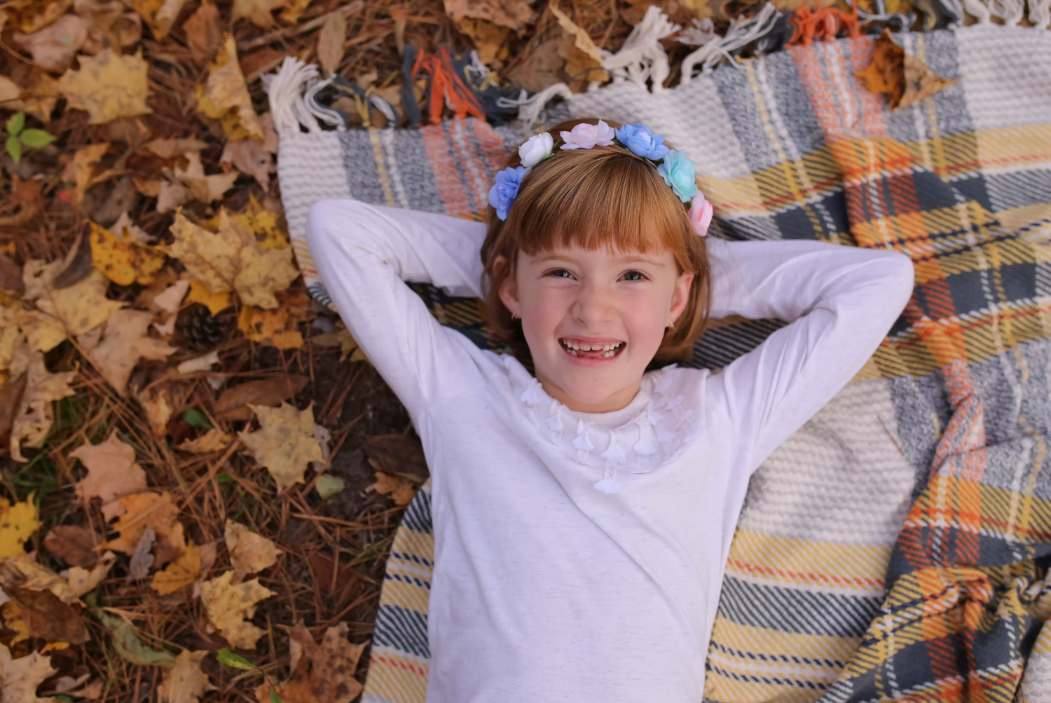 Children laying on a plaid blanket playing with autumn leaves.
