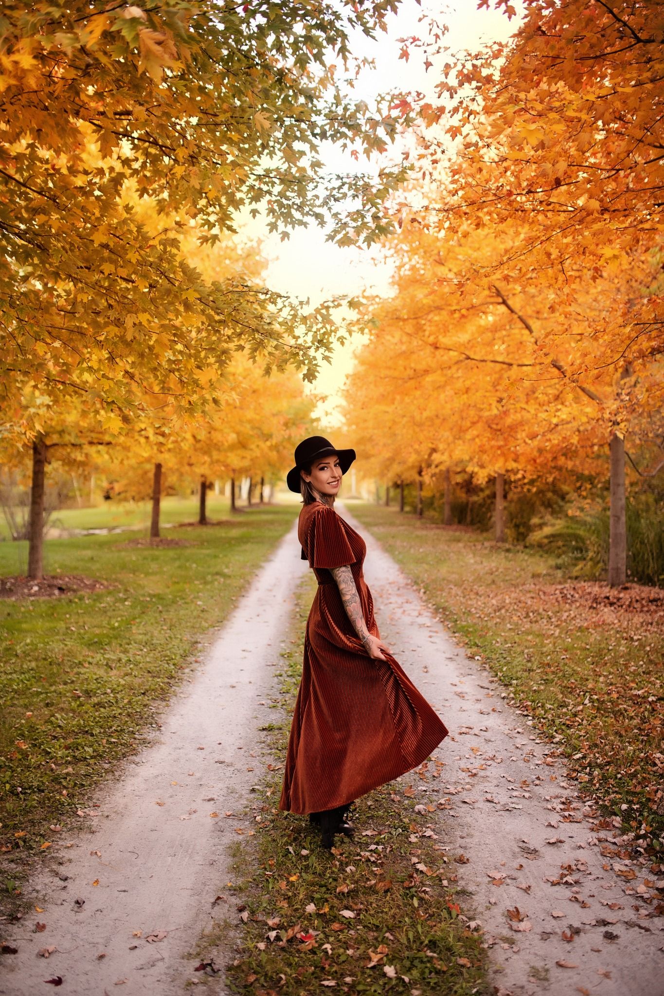 Dirt path through golden autumn trees with fallen leaves scattered on the ground.