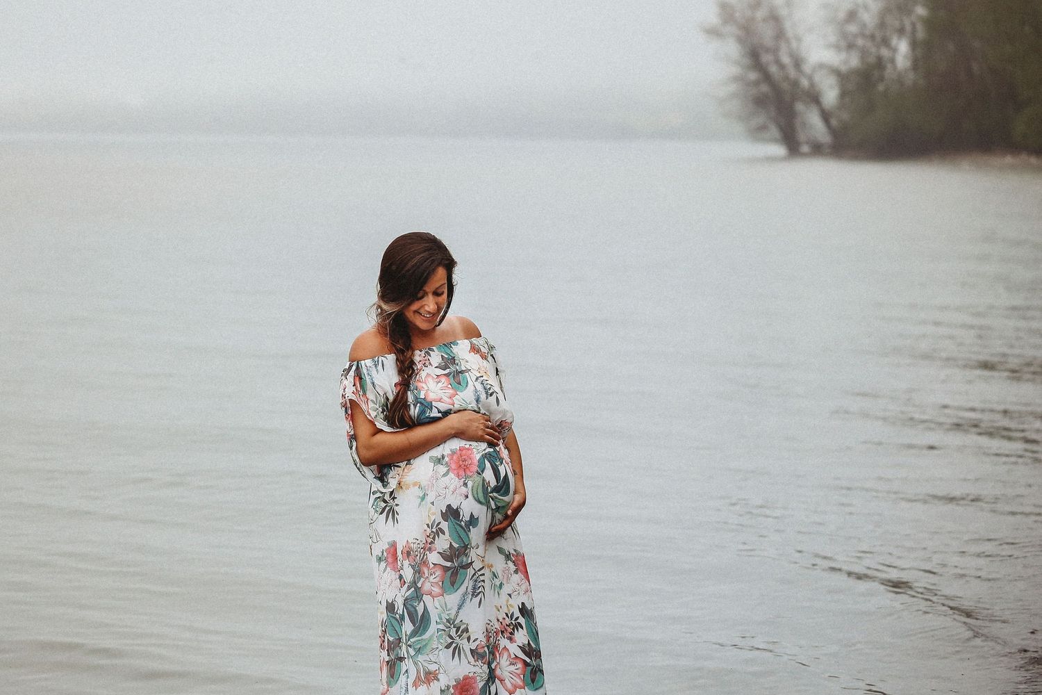A romantic couple in floral dress poses by a serene lakeside during a photo session.