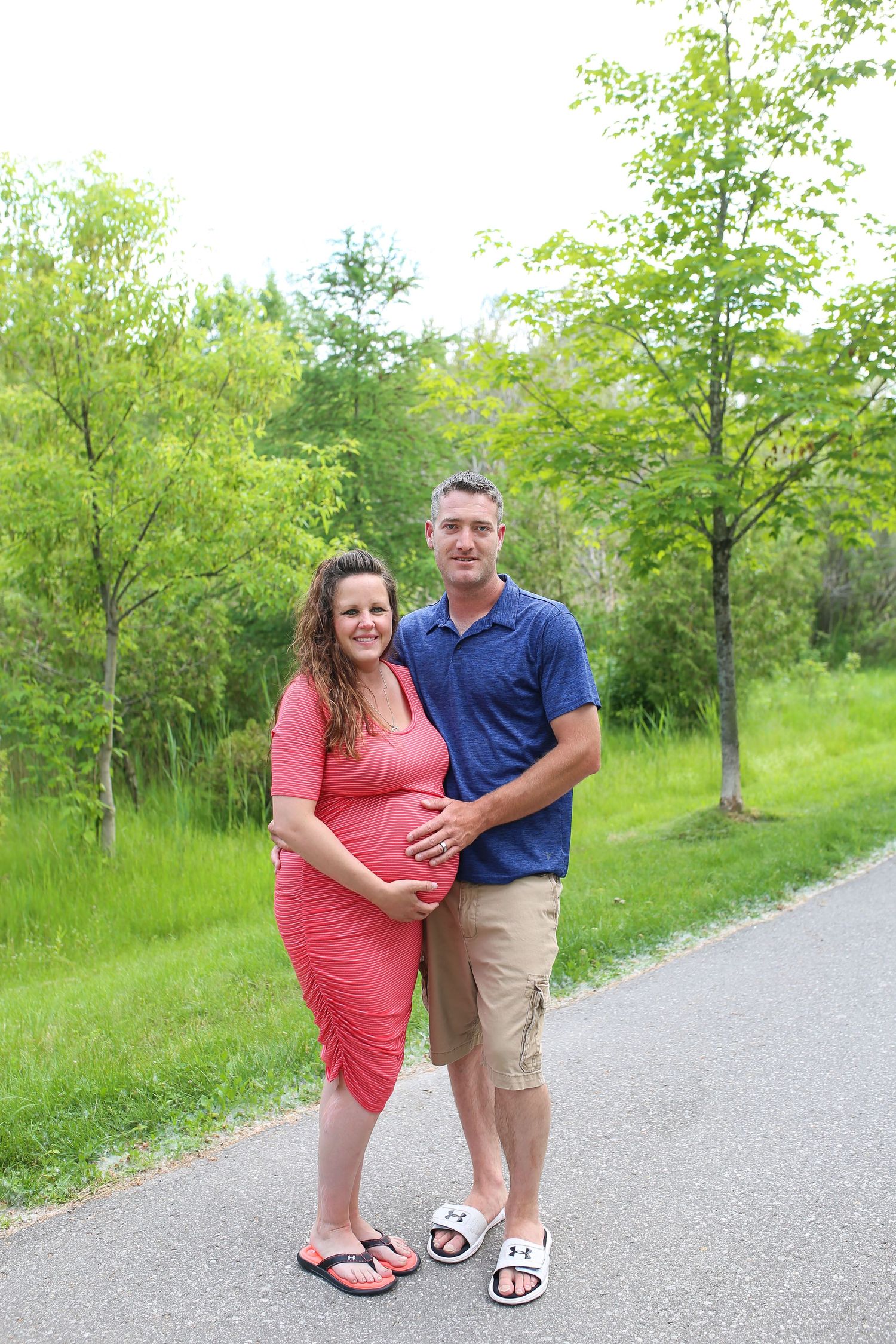 A couple poses on a paved path surrounded by lush green spring foliage.
