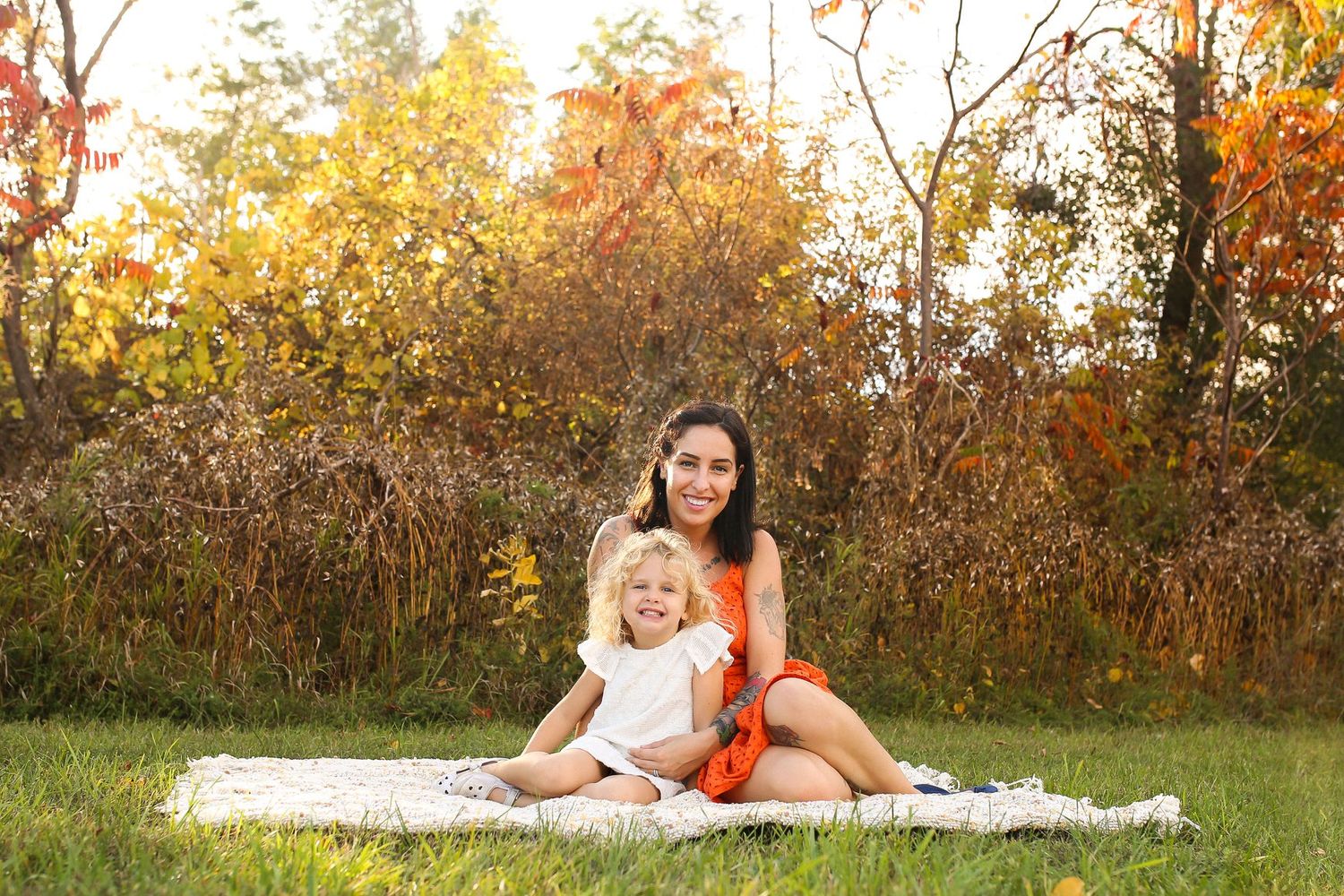 Family photoshoot in autumn setting with golden light filtering through trees.