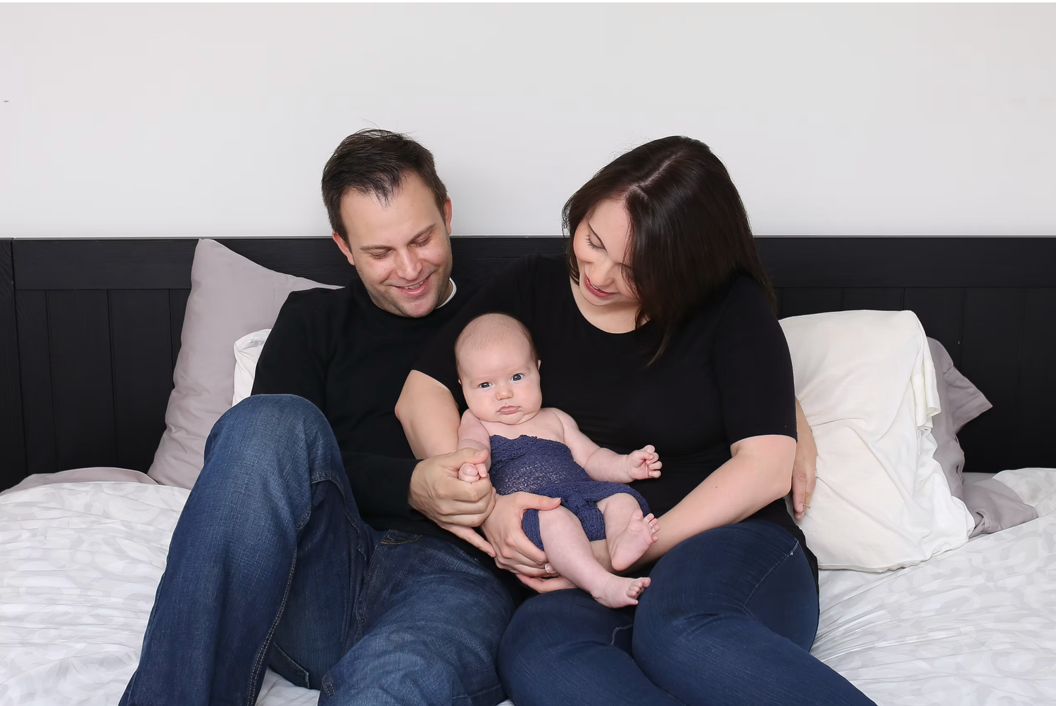 Intimate family moment captured on white bed with natural lighting.