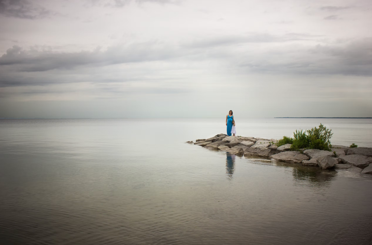 A solitary figure in blue stands on a rocky outcrop overlooking a misty lake.