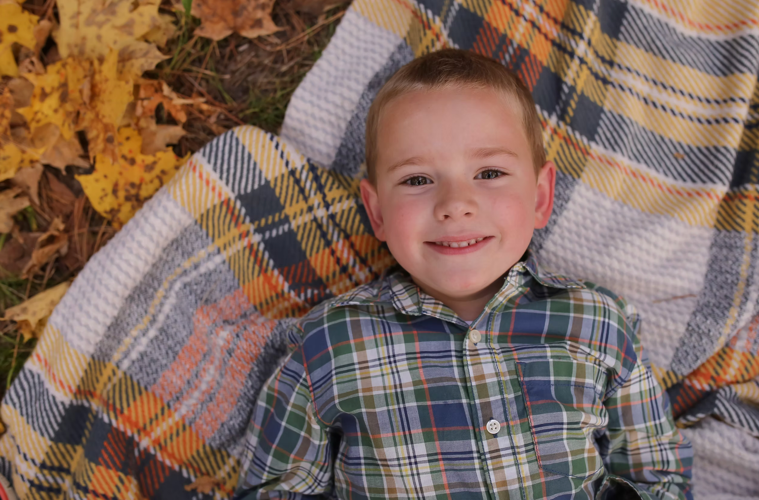 Cozy autumn portrait with plaid blanket and scattered orange leaves.