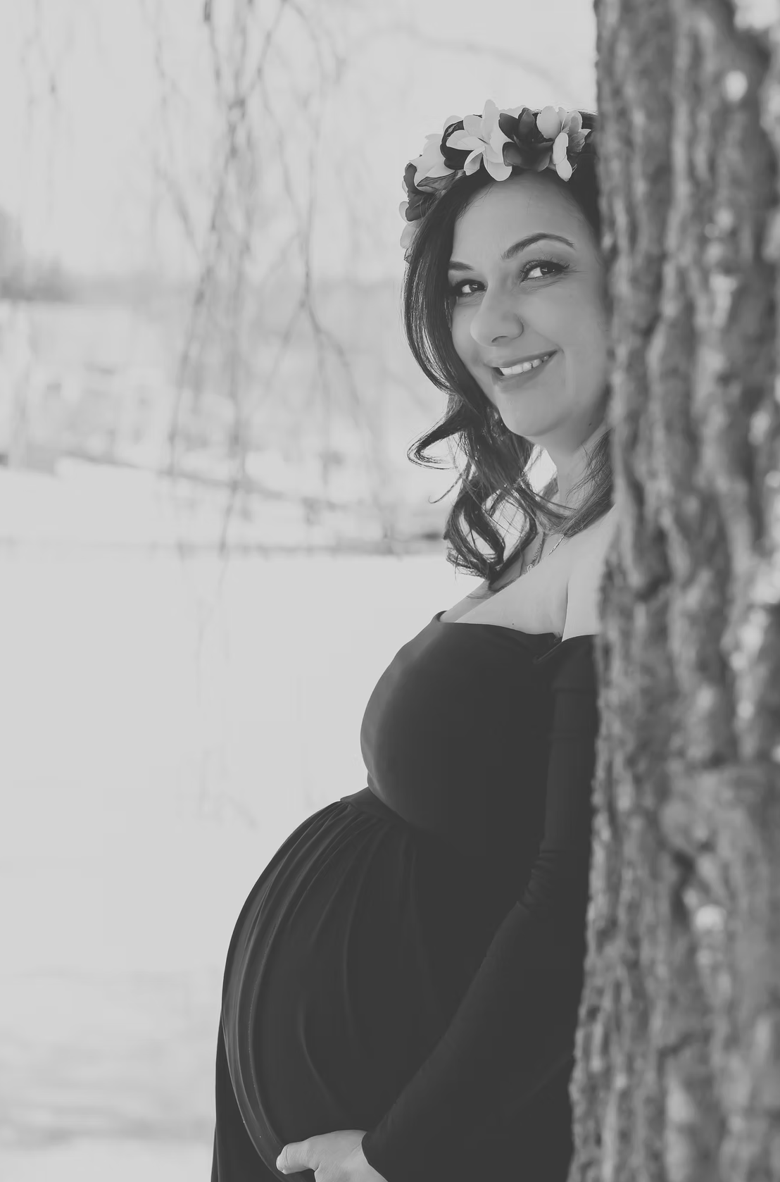 A winter maternity photo shoot in black and white with snow covered trees.