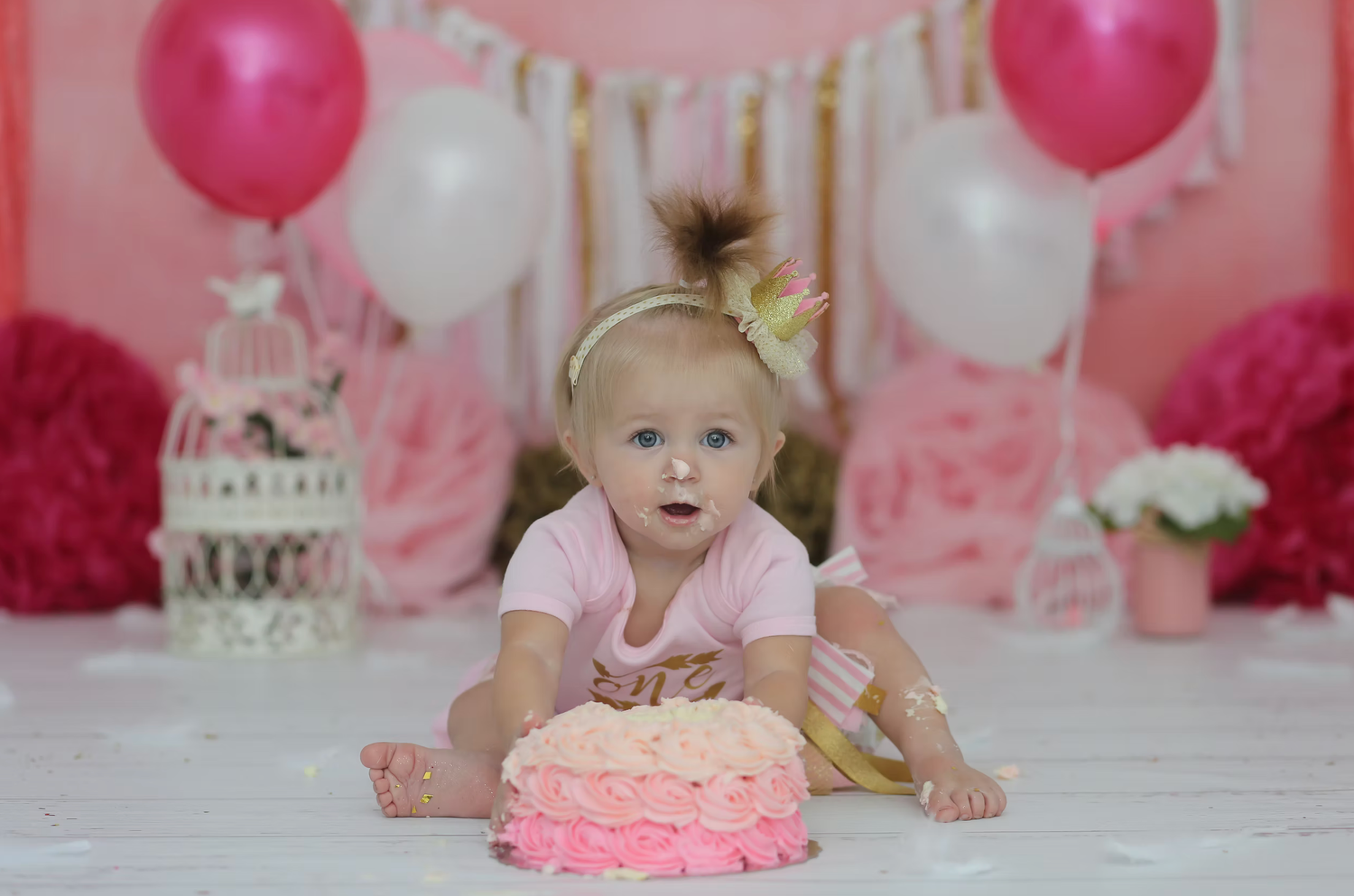 Pink and white balloon decorations with a smash cake setup for a first birthday celebration.