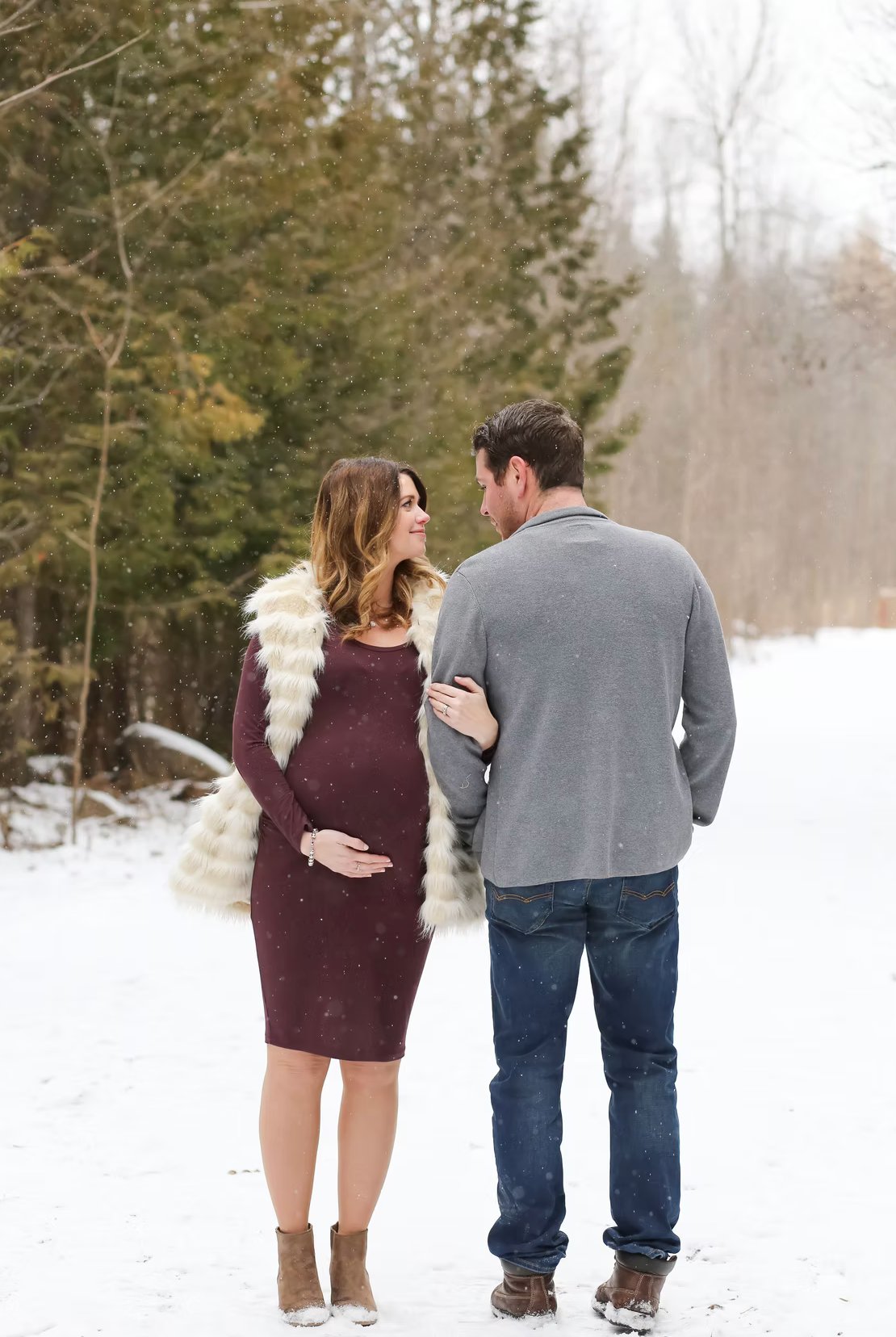 A couple embraces in a snowy winter scene wearing burgundy and grey clothing.