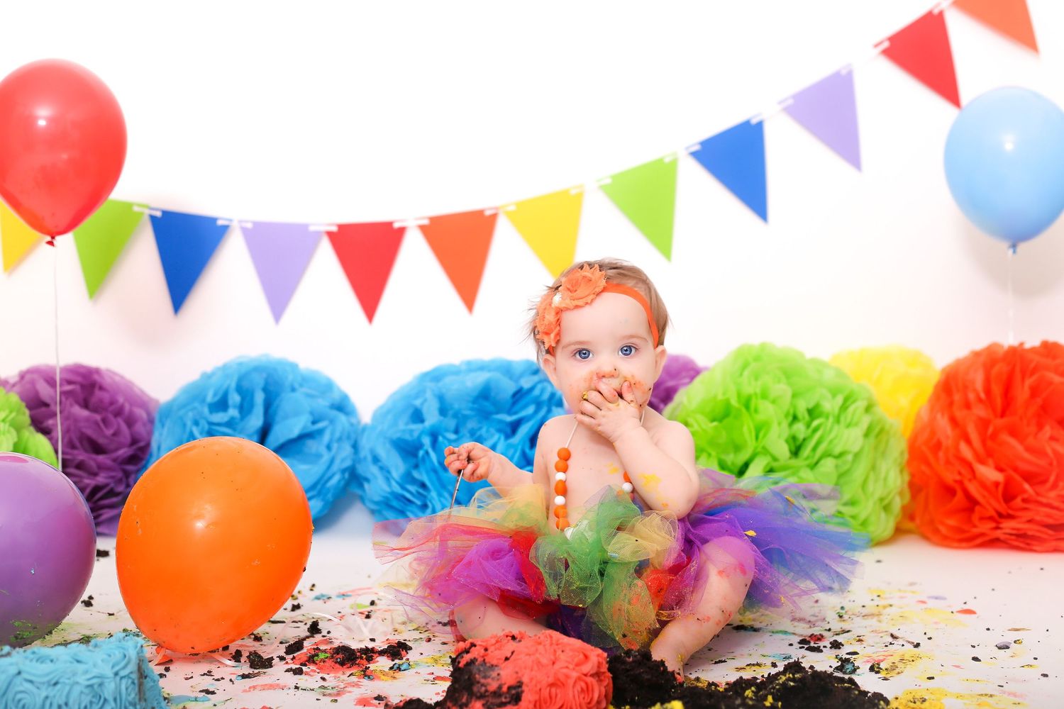 Party setup with multicolored triangle banners, balloons and decorative tissue paper flowers.