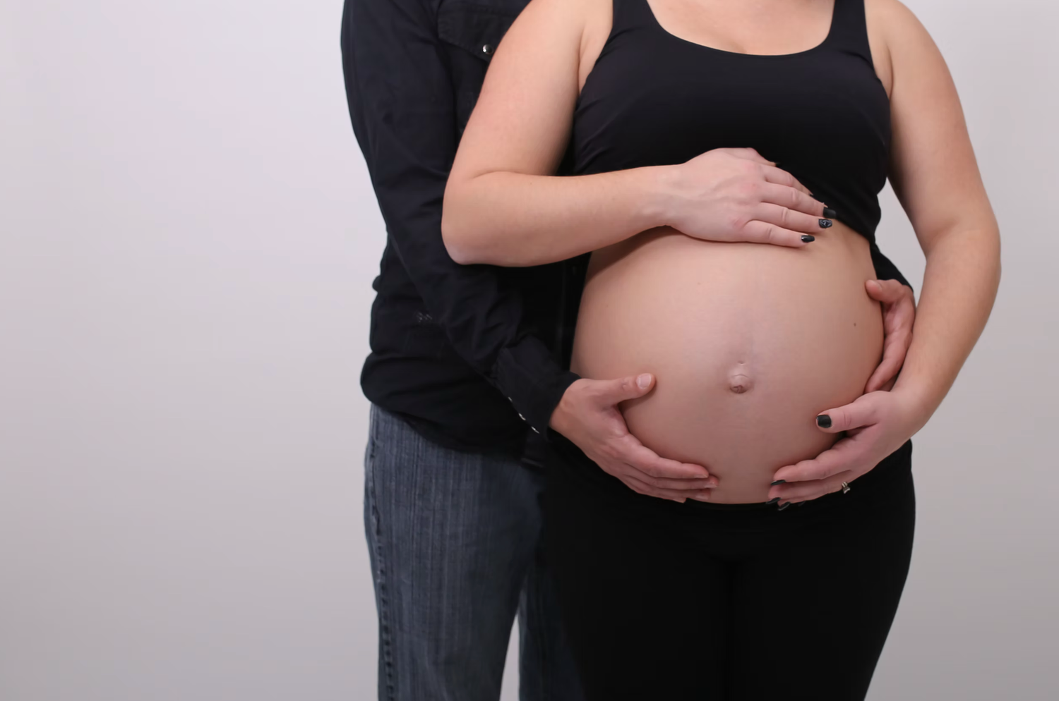 A tender maternity moment captured against a plain background.