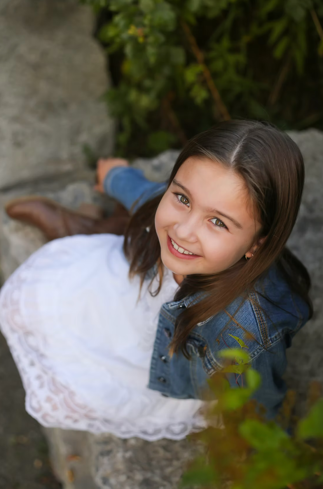 Portrait in white dress and denim jacket against natural stone background.