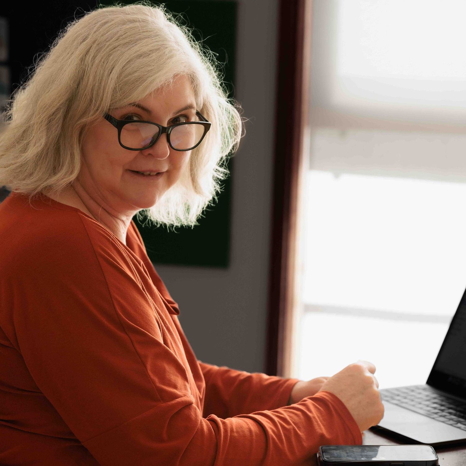 woman looking at camera, working on laptop