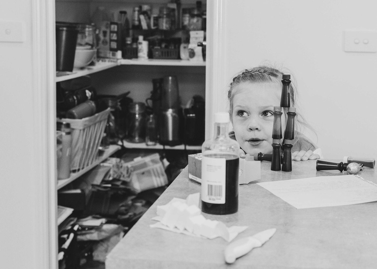 Candid image of young girl looking over kitchen bench top. Leigh Ball. documentary photographer.