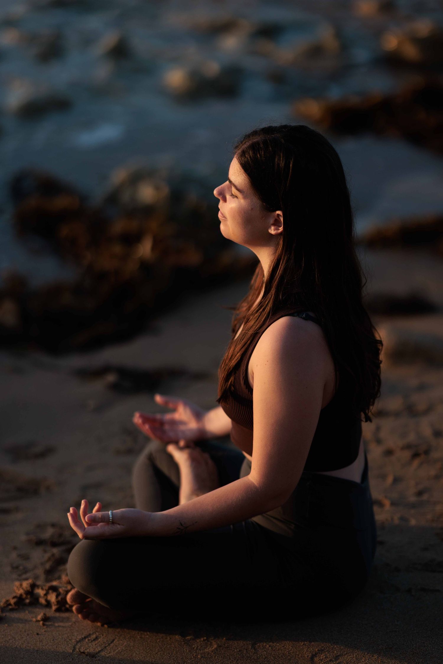 young woman practicing meditating at the beach at sunrise