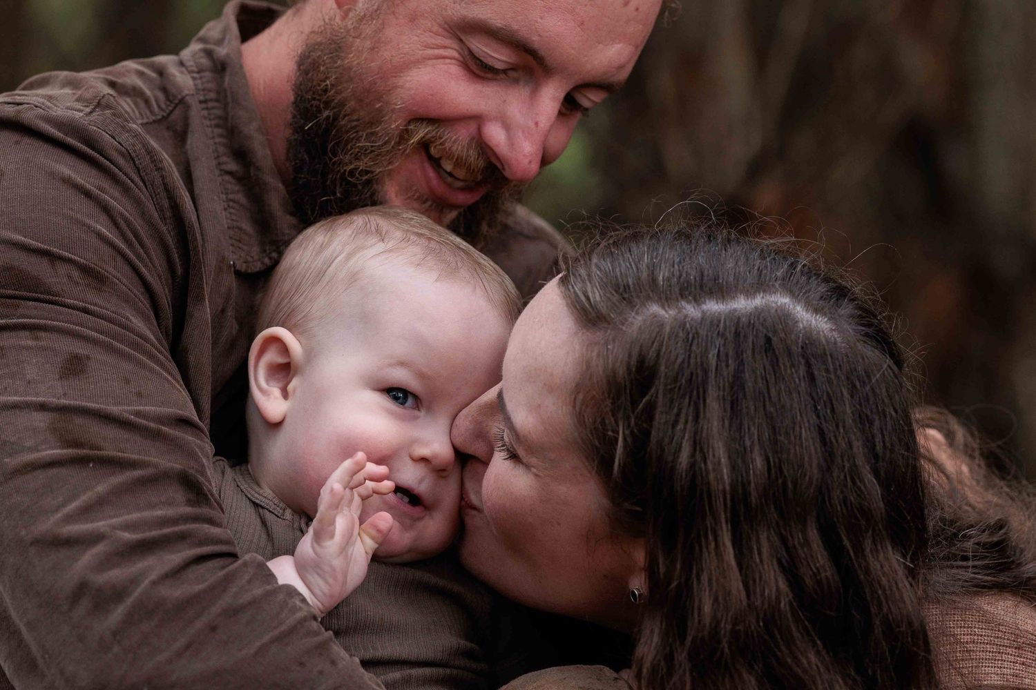 Mum, Dad and young boy cuddling while mum gives the boy a kiss on the cheek. Riddell's Creek, Victoria.