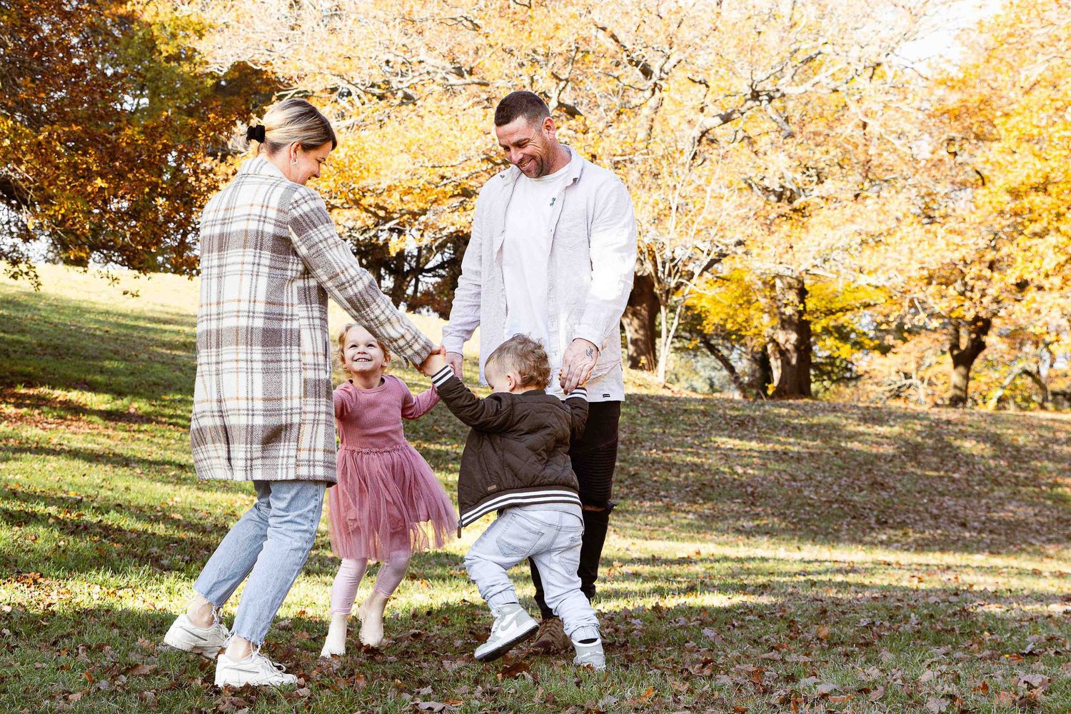 Mum, Dad and two young children play a game in the park. Gisborne, Victoria in Autumn