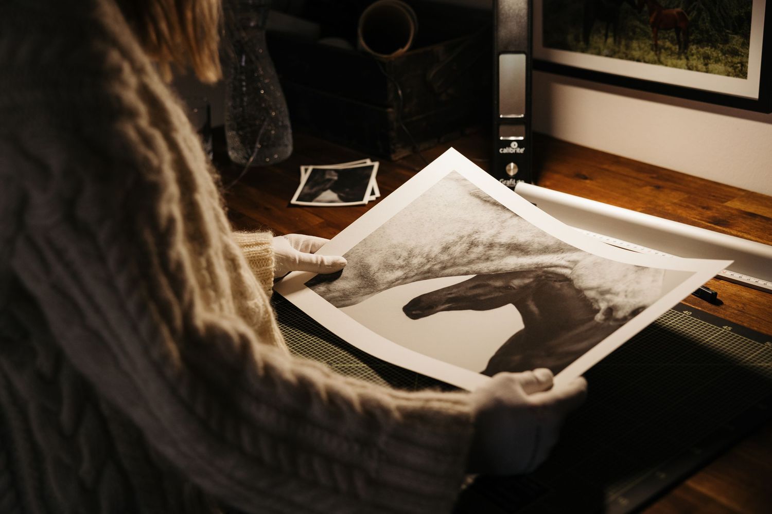 Person in knit sweater holding a black and white fine art photograph of a horse in a warmly lit studio.